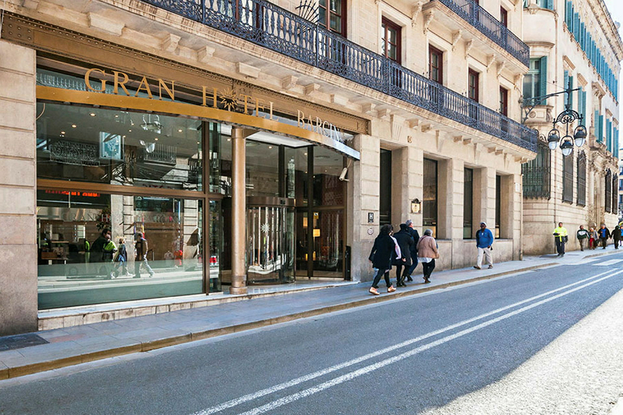 En gate med bygninger og inngangen til et hotell med skiltet "Gran Hotel Barcino". (AI-generert tekst)
