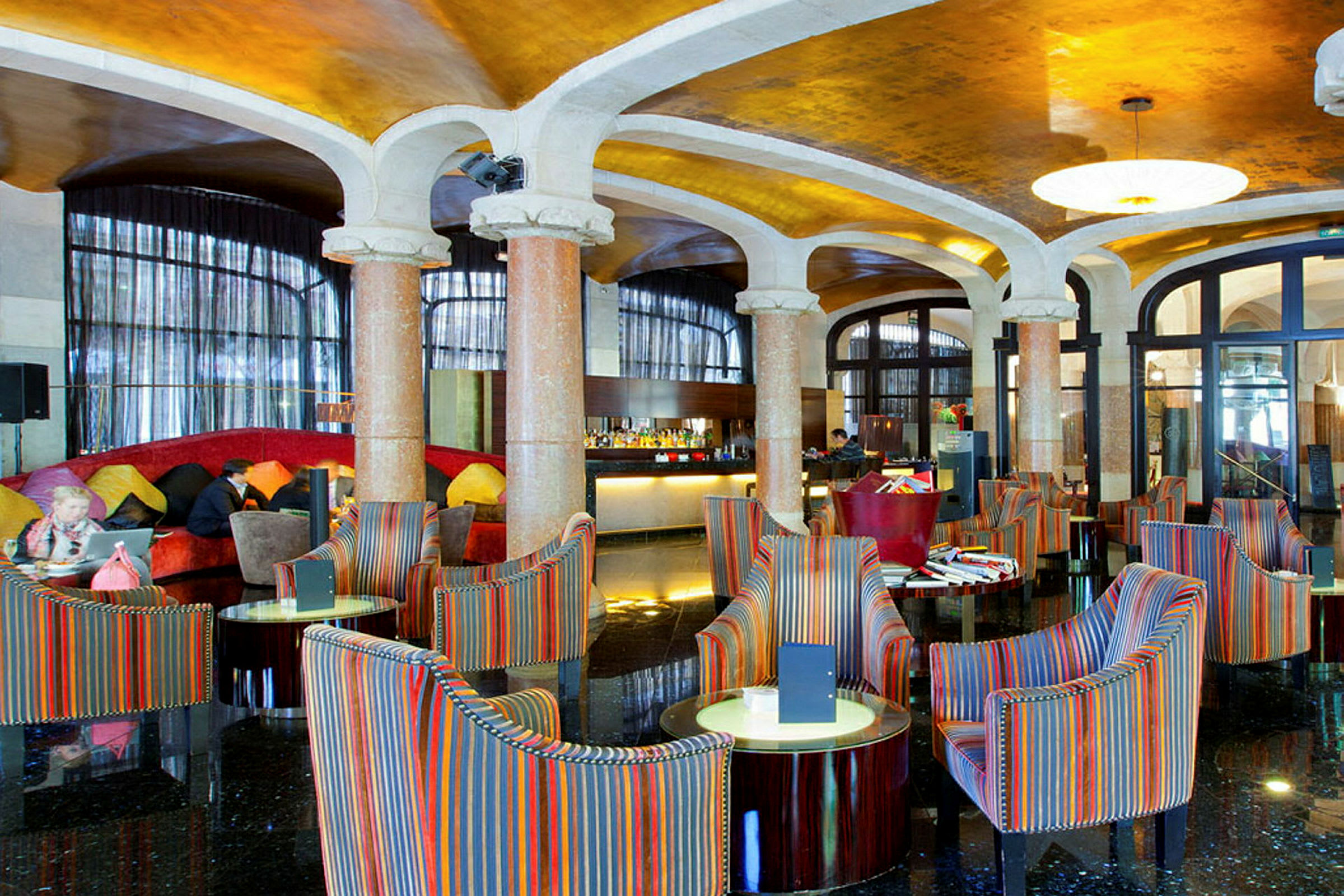 Et elegant hotellobbyområde med fargerike lenestoler og runde bord, marmorsøyler og et skinnende gulv. (AI-generert tekst)