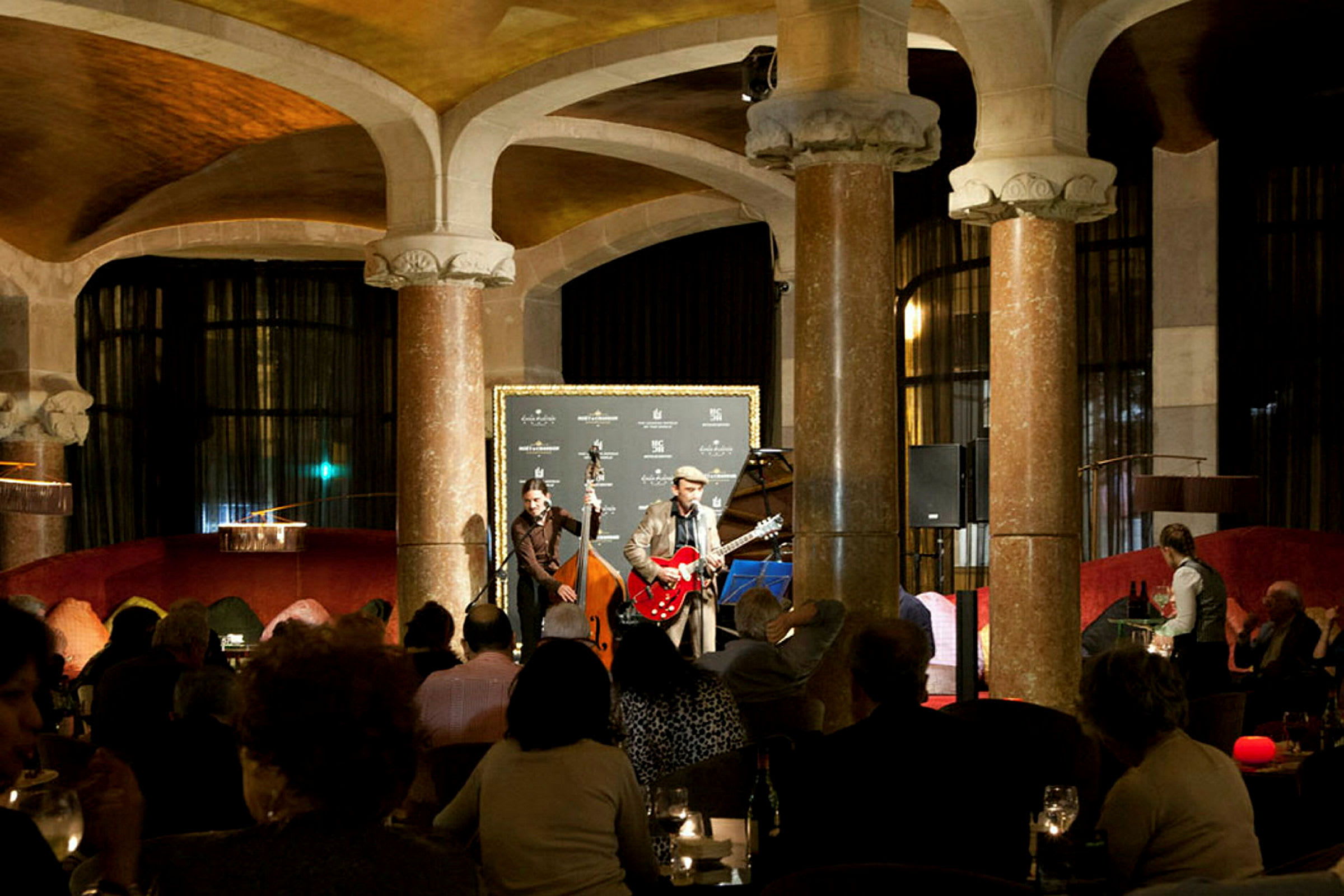 En innendørsscene der musikere opptrer foran et sittende publikum i en elegant setting. (AI-generert tekst)