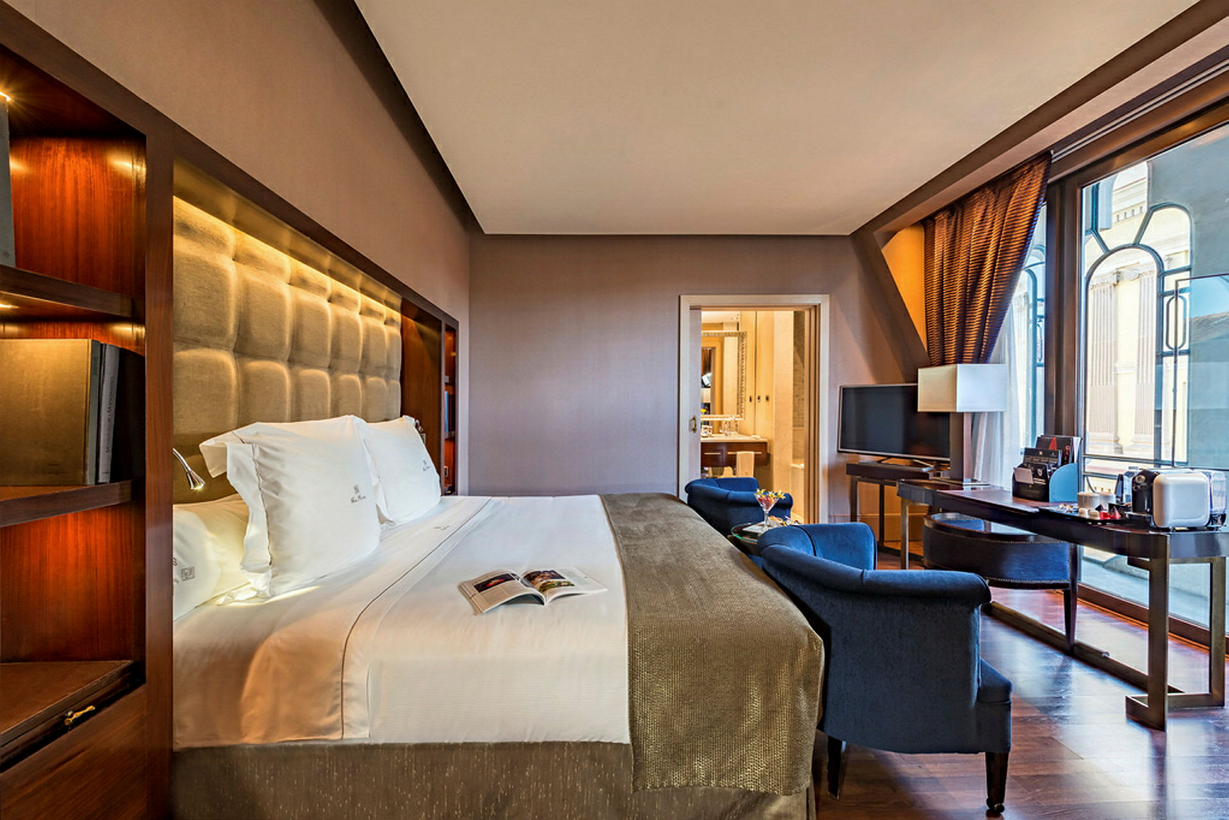 Et moderne og velordnet hotellrom med en stor seng, lenestoler, et skrivebord og store vinduer. (AI-generert tekst)