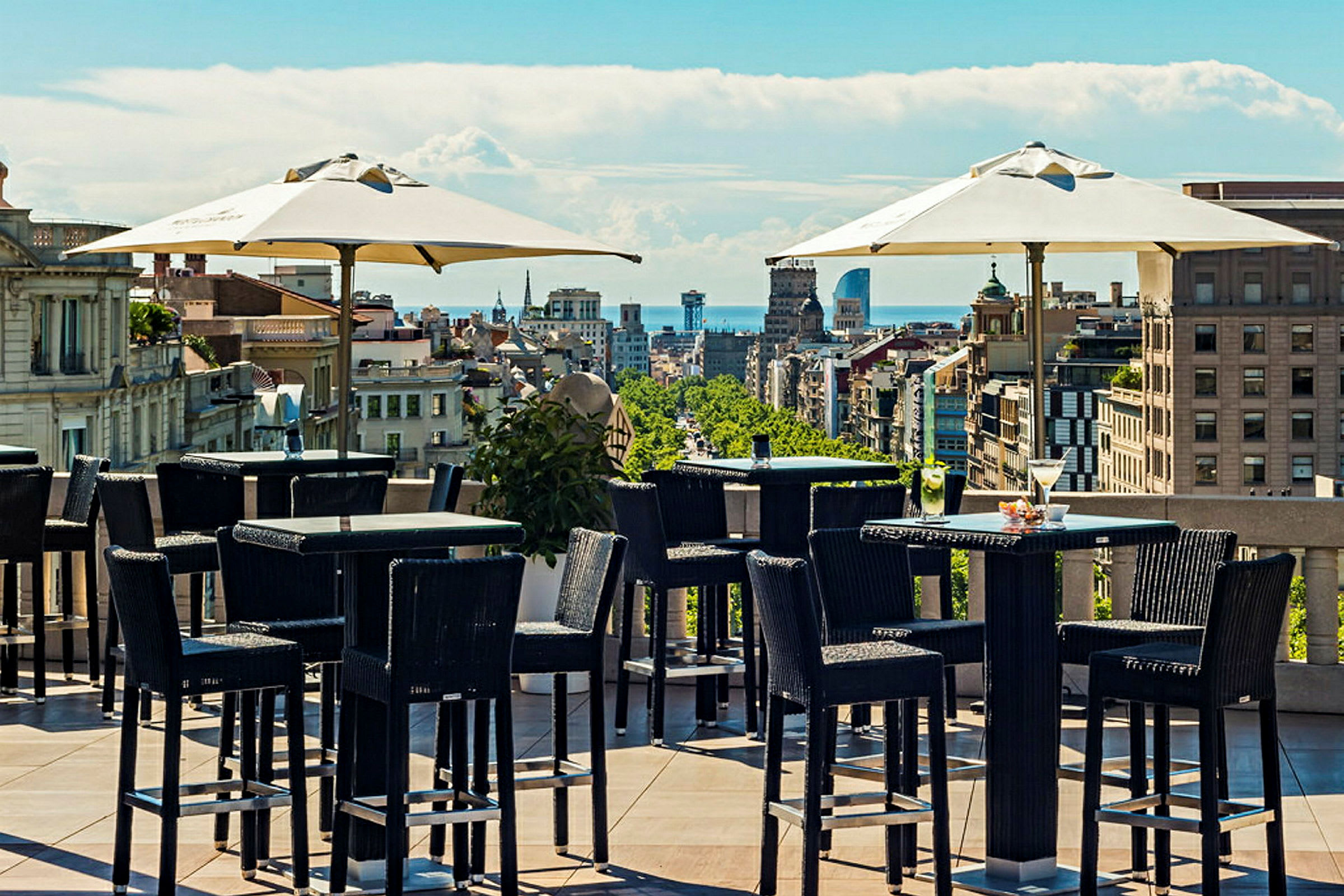 Utendørs servering på en takterrasse med utemøbler og utsikt over byens silhuett under en klar blå himmel. (AI-generert tekst)