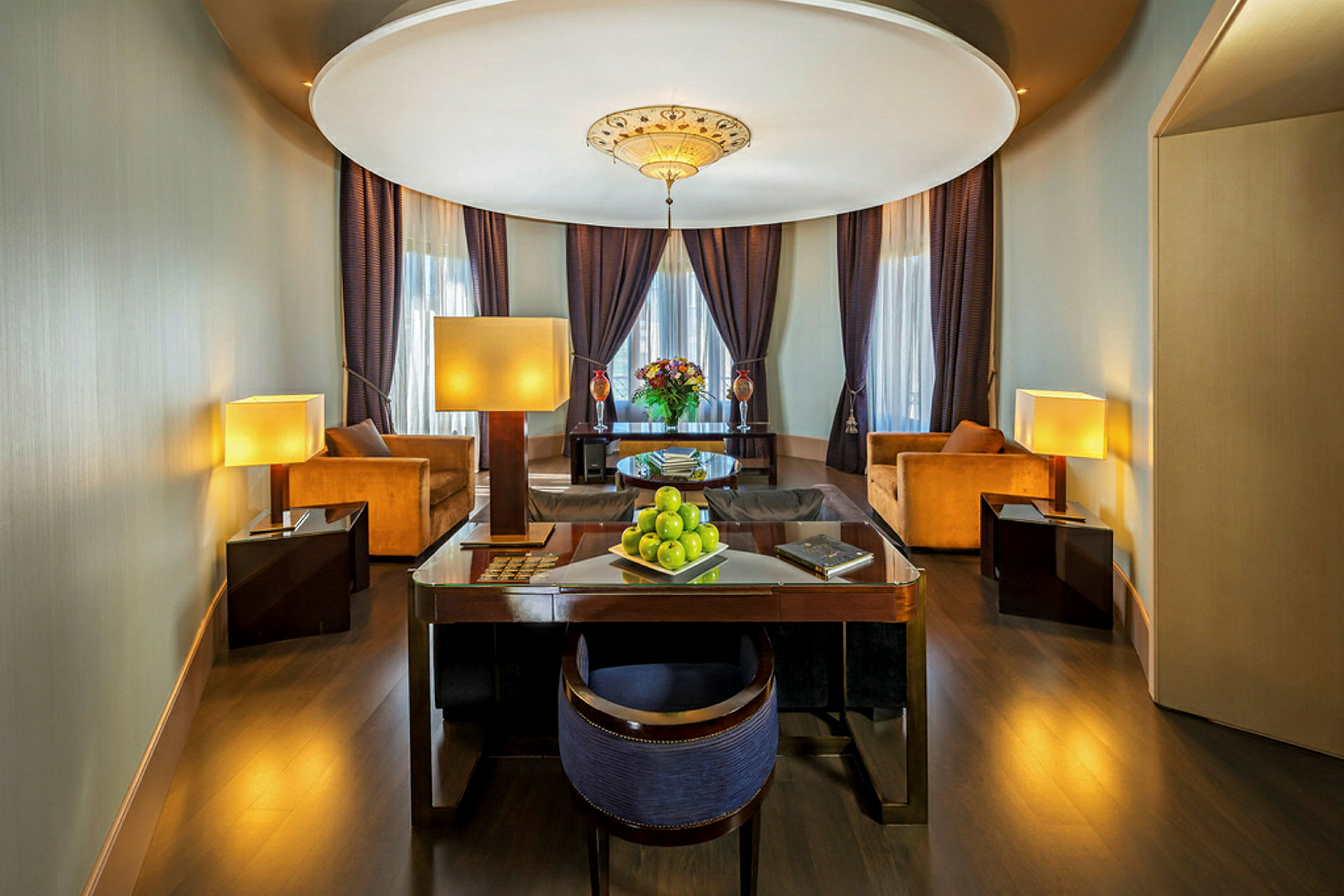 Et elegant hotellrom med sittegruppe, skrivebord, sofaer, lamper og stemningsfull belysning. (AI-generert tekst)