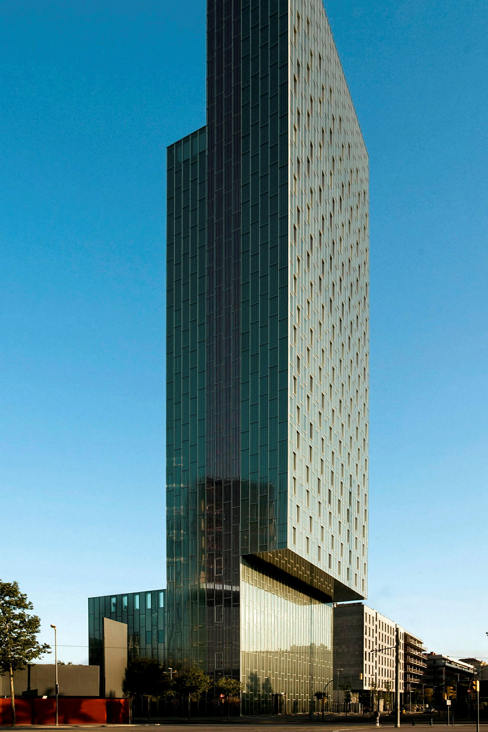 Høy bygning med moderne arkitektur omgitt av blå himmel og urbane bygninger. (AI-generert tekst)