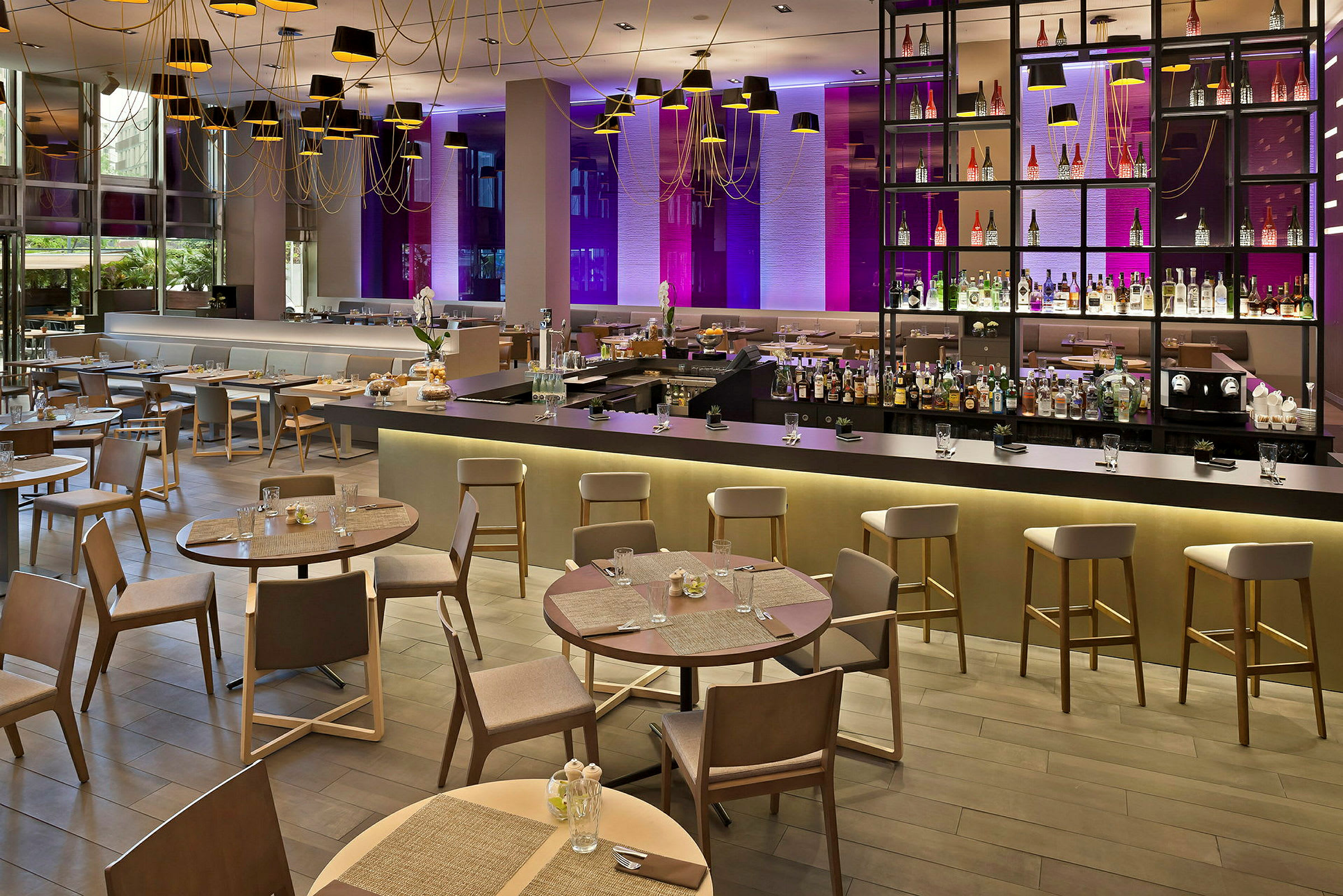 Bilde av en moderne restaurant med elegante bord og stoler, en lang bardisk og en dekorativ bakvegg med flasker samt belysning. (AI-generert tekst)