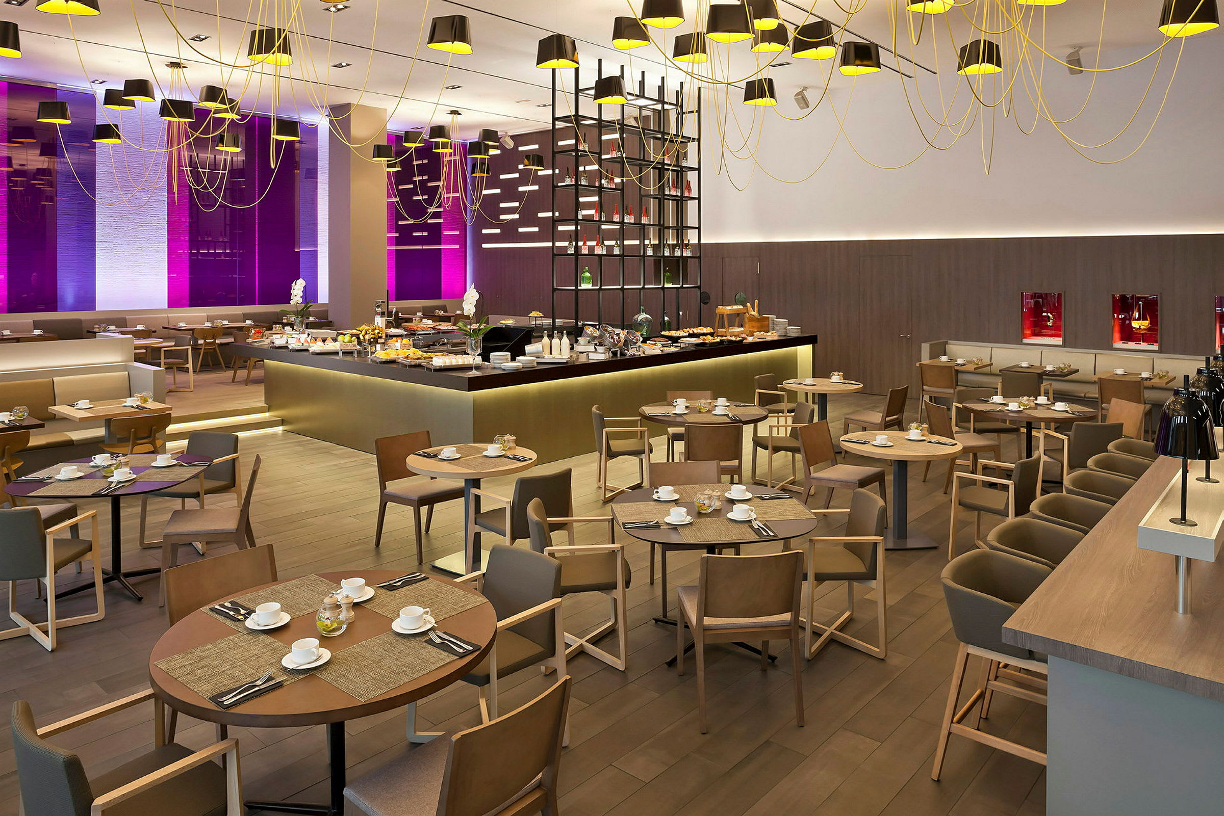 En restaurantinteriør med spisebord og stoler samt en matserveringsområde omgitt av moderne belysning og innredning. (AI-generert tekst)