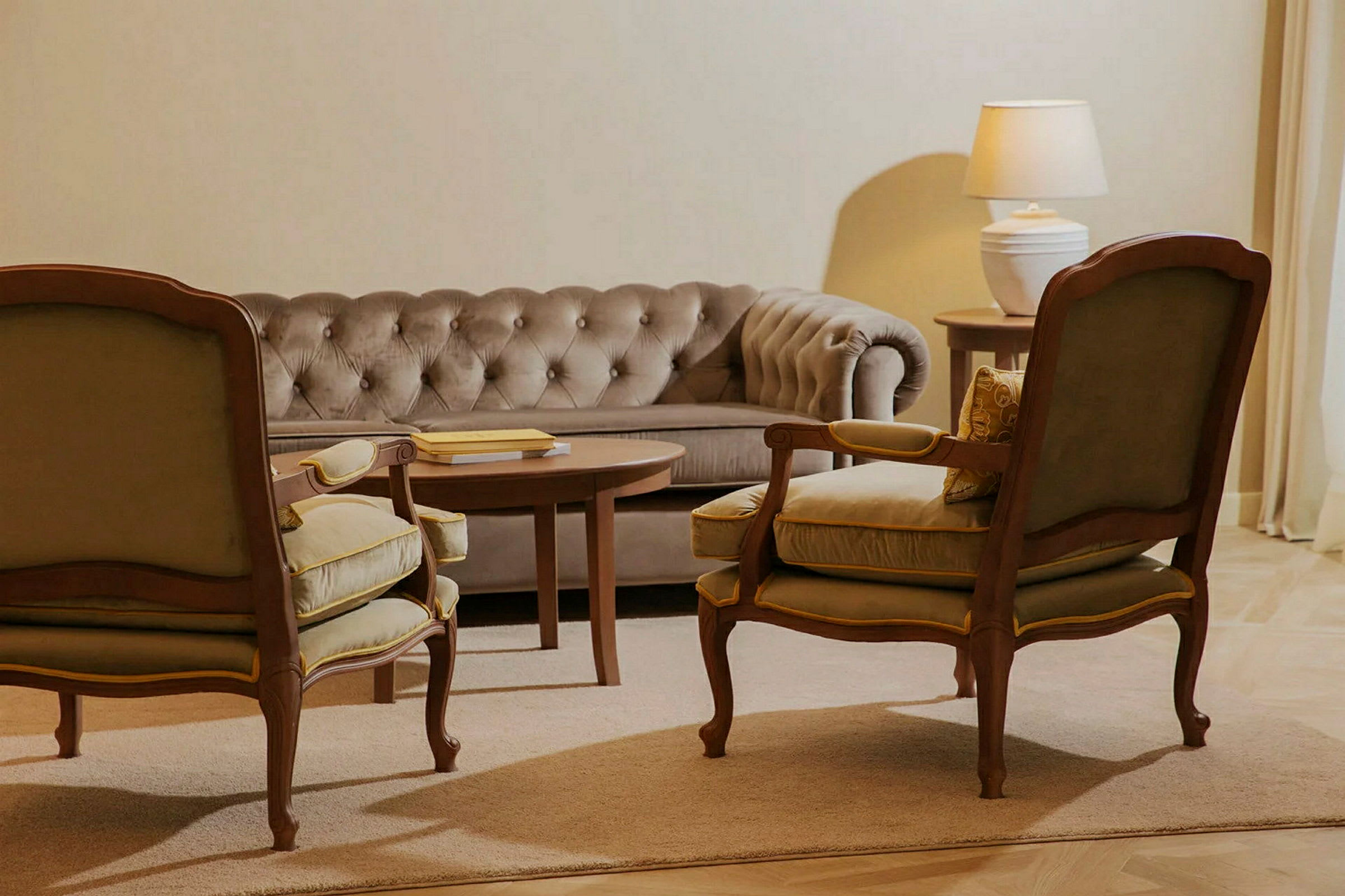En sittegruppe med en beige sofa, to lenestoler og et sofabord. En lampe på et sidebord er synlig i bakgrunnen. (AI-generert tekst)