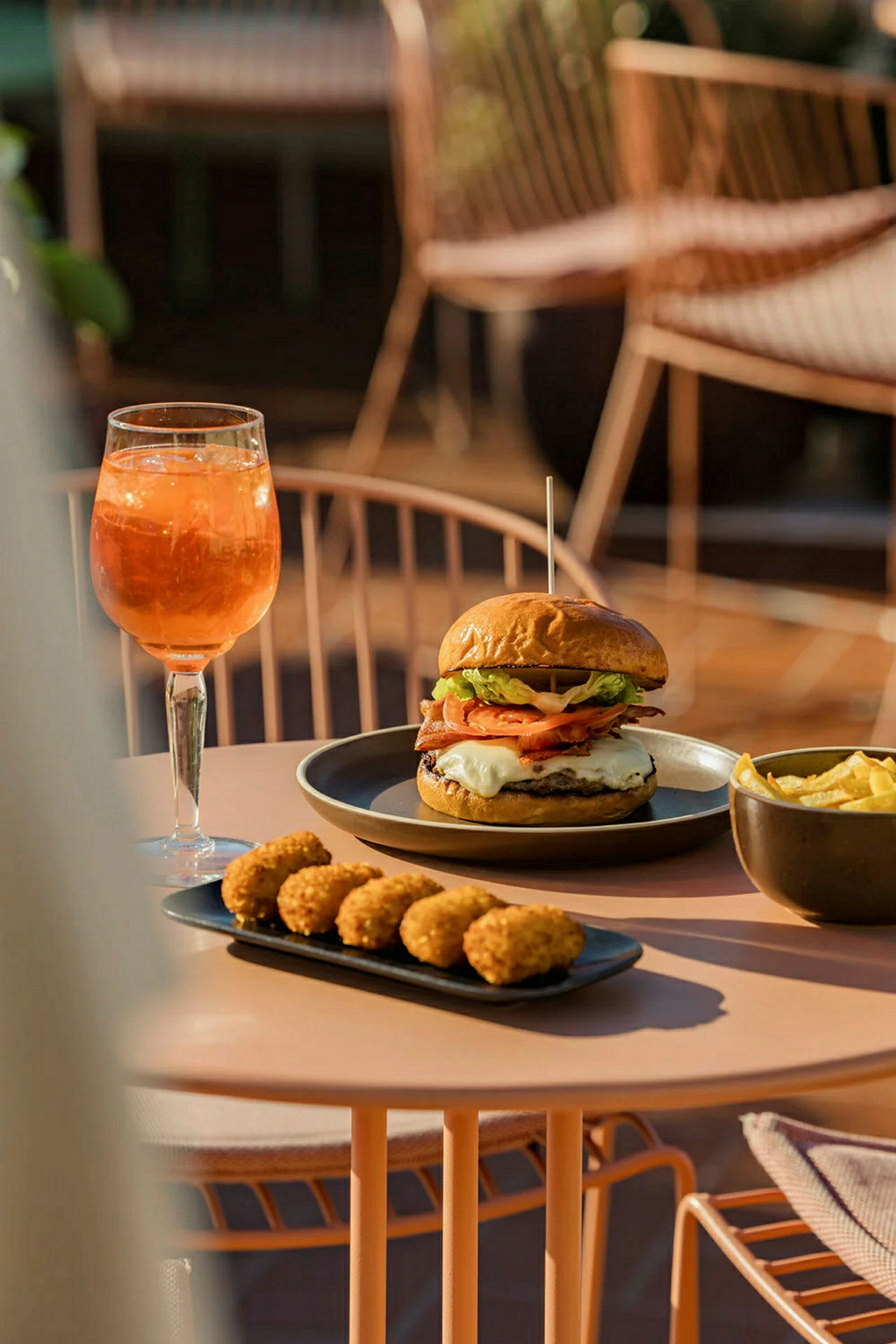 En tallerken med hamburger og pommes frites, ved siden av et fat med små snacks og et glass oransje drikke. (AI-generert tekst)