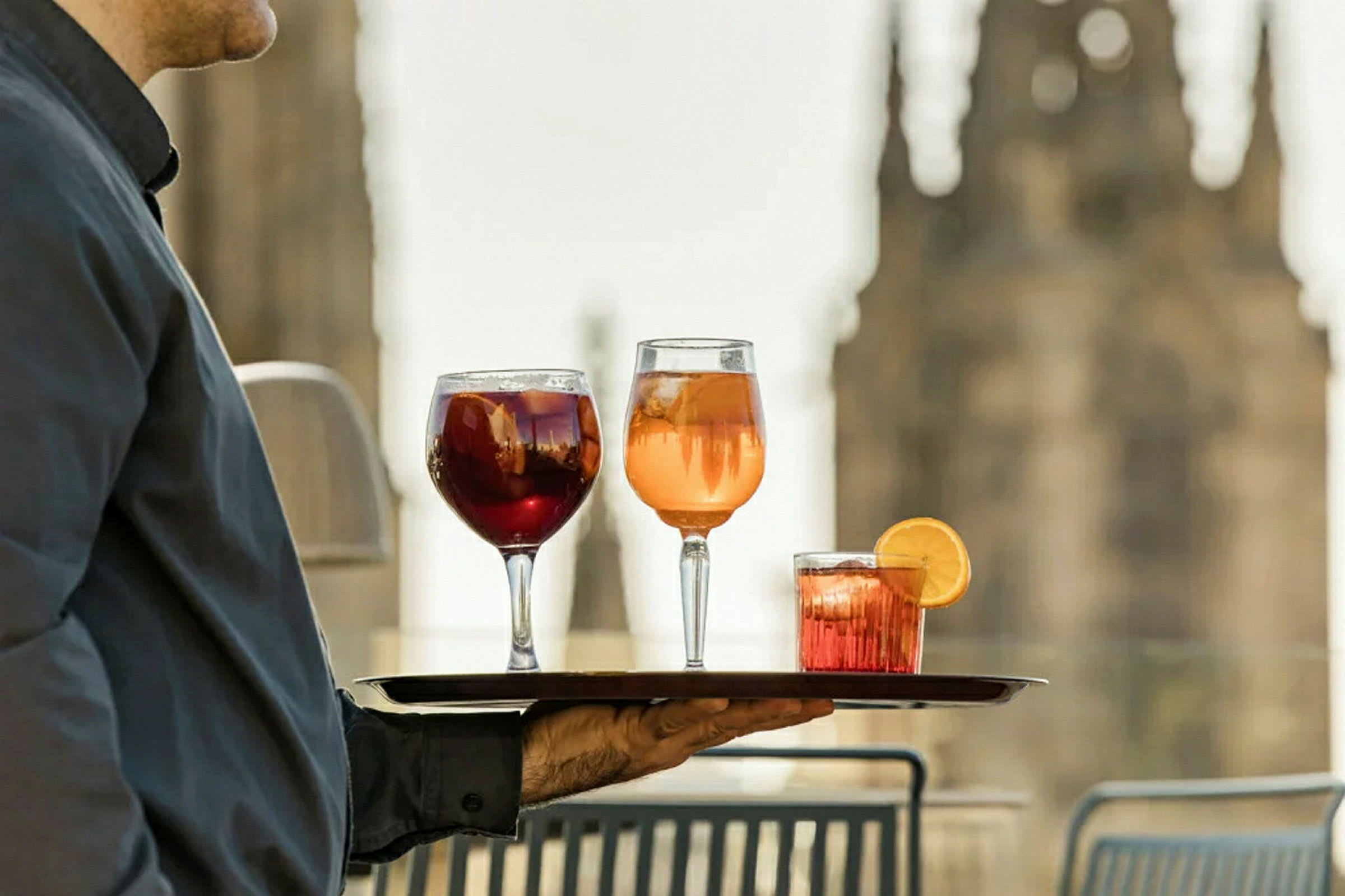 En hånd holder et brett med tre glass med drinker. (AI-generert tekst)