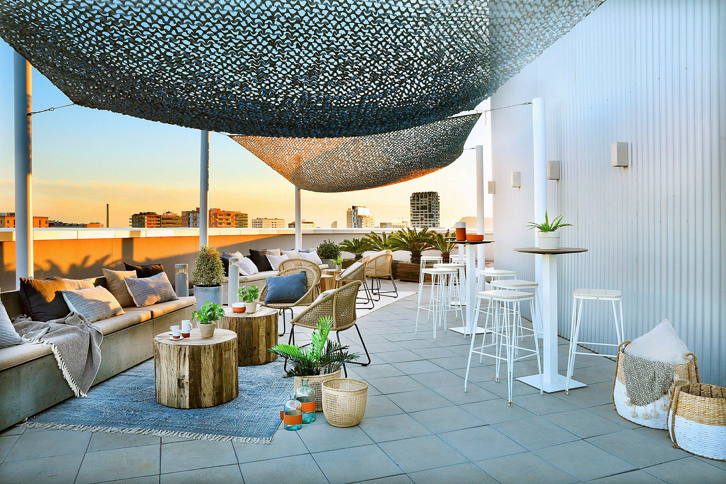 En moderne takterrasse med sitteplasser, bord og dekorasjoner. En solskjerm henger over, og byen vises i bakgrunnen. (AI-generert tekst)