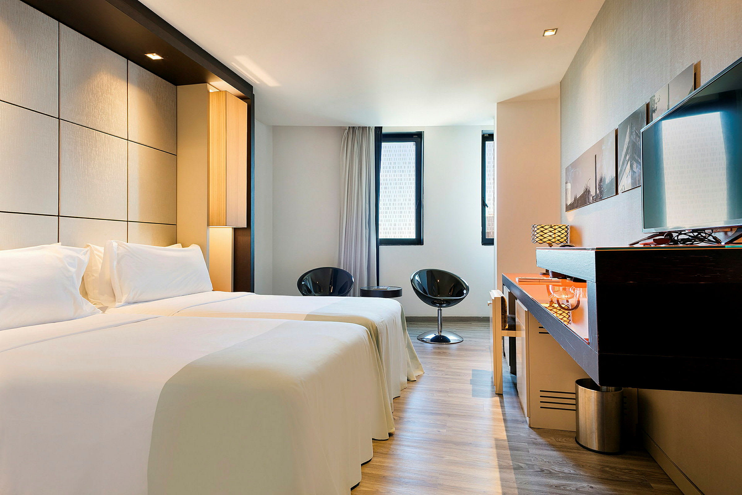 Et moderne hotellrom med to enkeltsenger, liten sittegruppe og skrivebord. (AI-generert tekst)