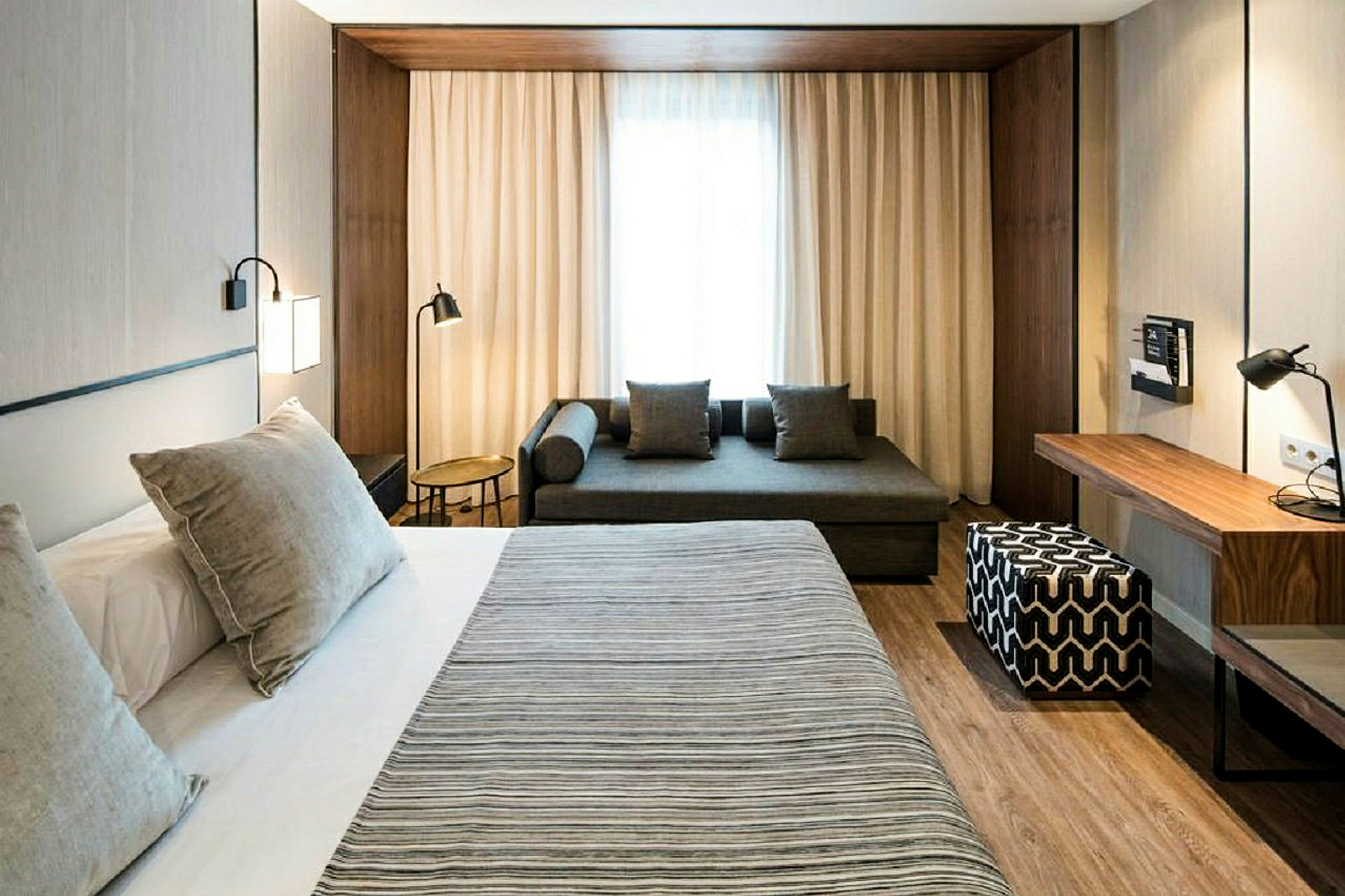 Et moderne hotellrom med en stor seng, sofa og skrivebord. (AI-generert tekst)
