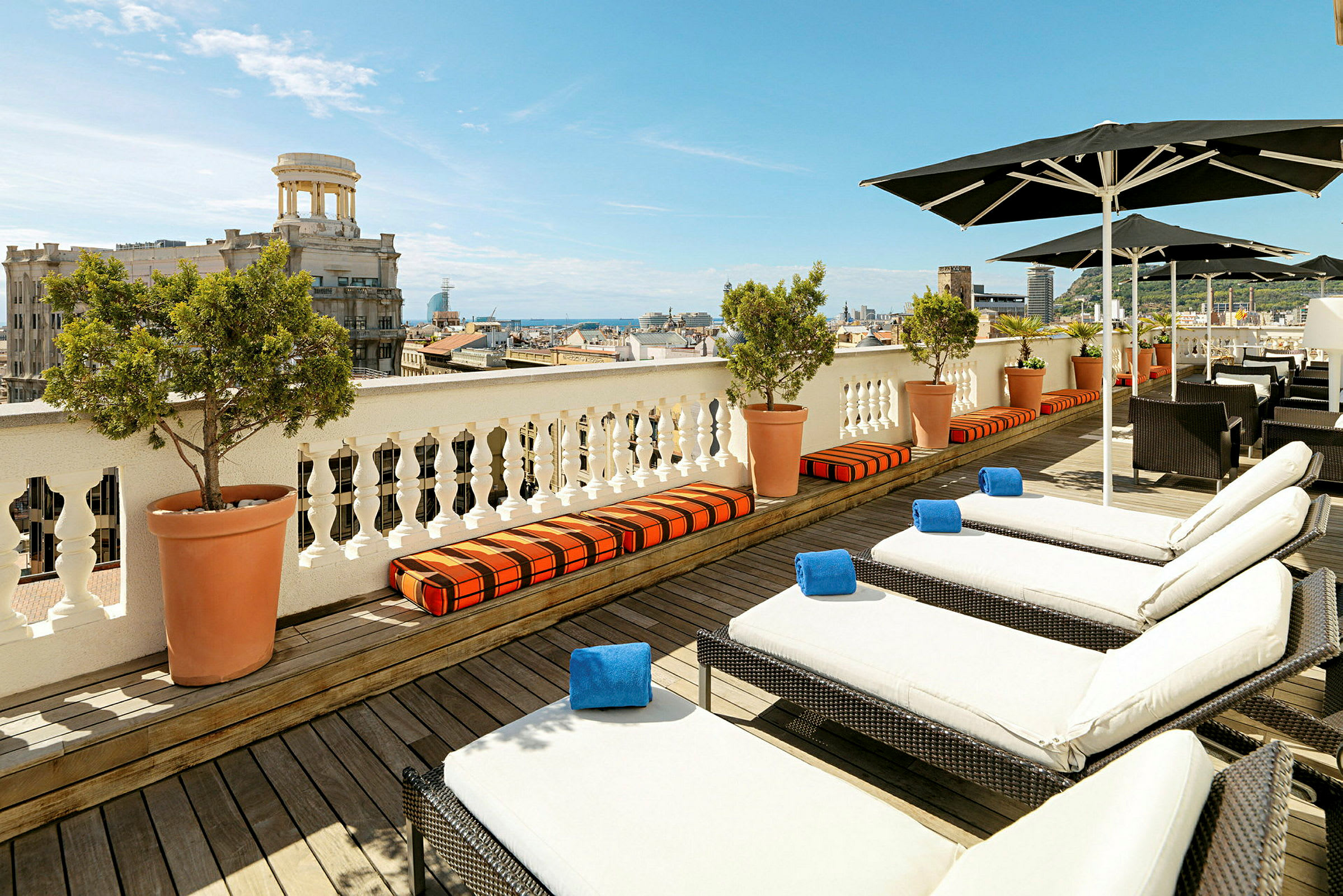 Utsikt over en terrasse med solsenger og parasoller, med en by og havet i bakgrunnen. (AI-generert tekst)