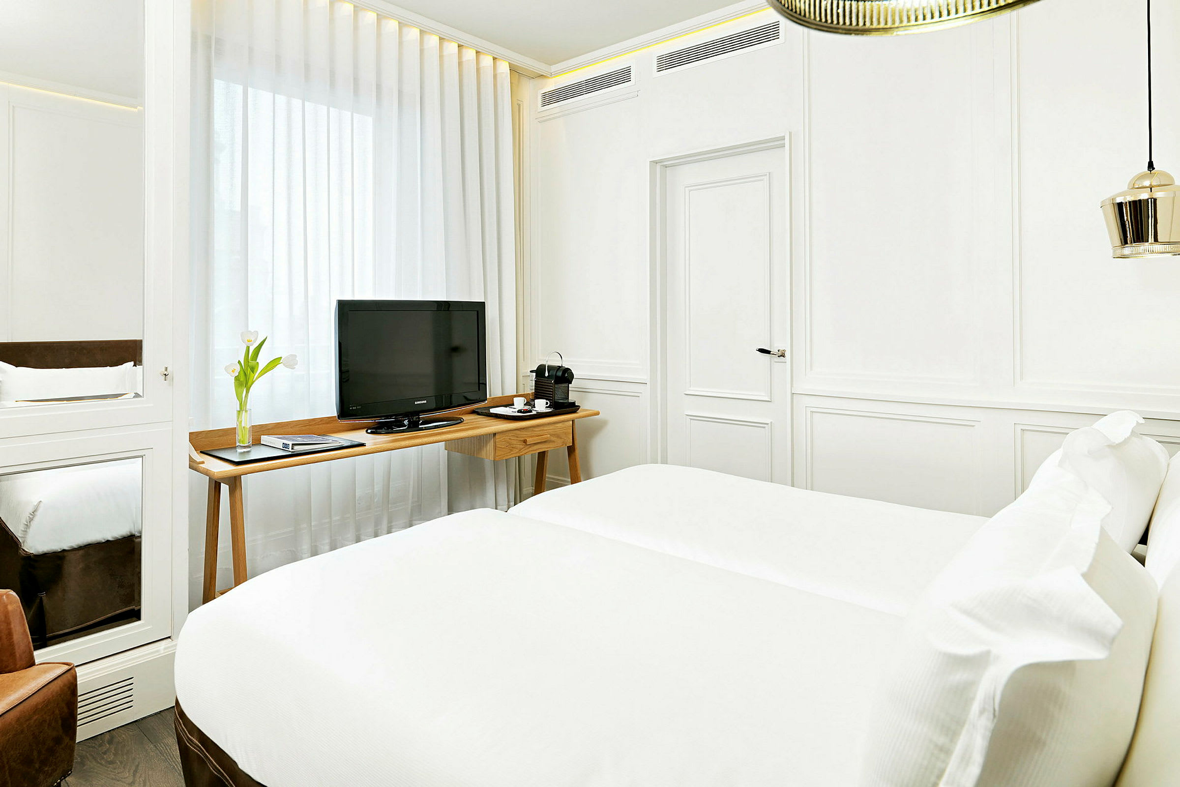 Et lyst innredet hotellrom med hvit farge, en dobbeltseng, en TV på et trebord og en kaffemaskin. (AI-generert tekst)