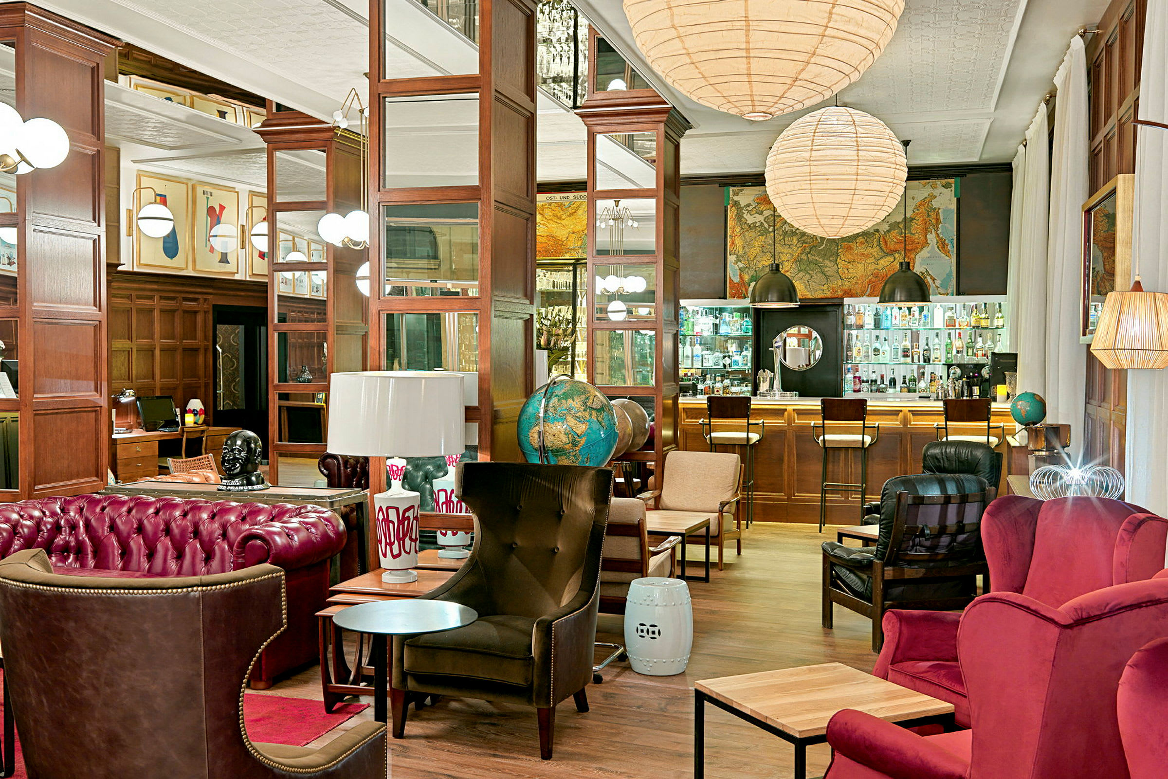 En stilfull lounge med røde og brune møbler, globuser, kunstverk på veggene og en bar med glassdisk i bakgrunnen. (AI-generert tekst)