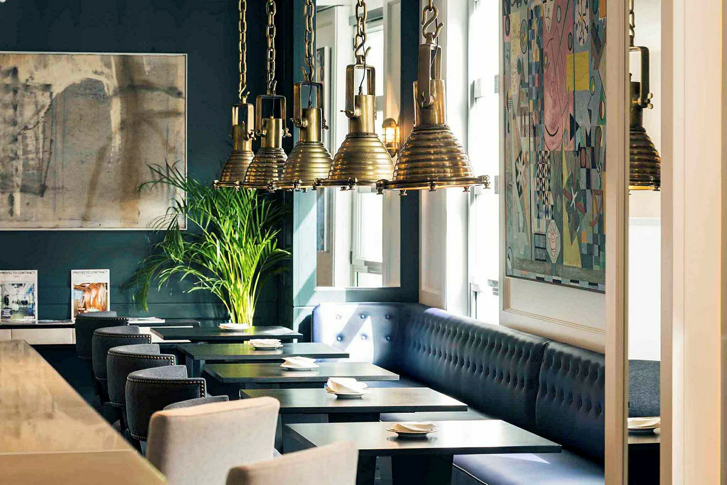 Interiør av en restaurant med mørkeblå vegger, kunstverk, hengende lamper og sitteplasser ved bord. (AI-generert tekst)