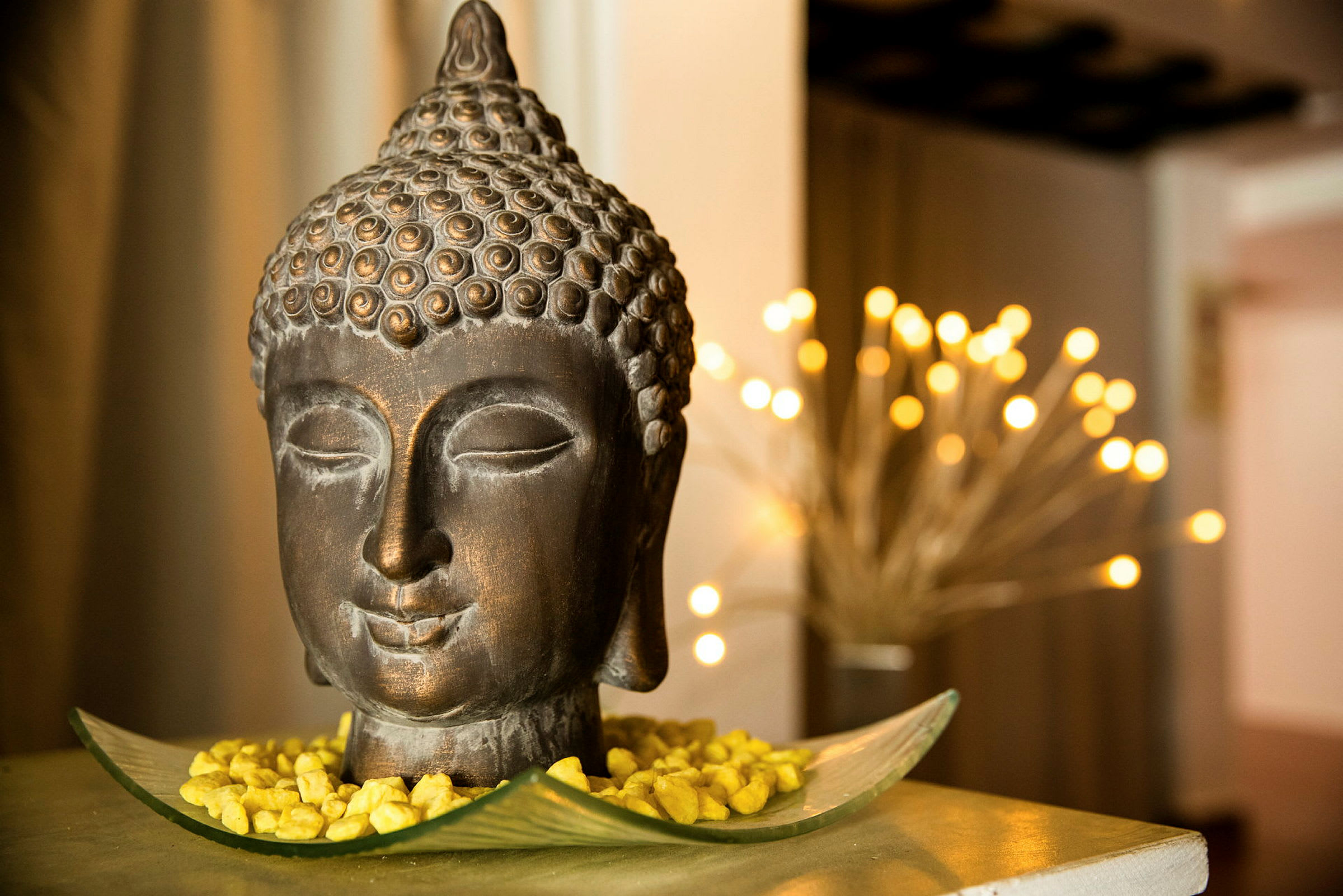En dekorativ Buddhastatuett plassert på et fat med gulldekorative steiner. Mykt lys i bakgrunnen. (AI-generert tekst)