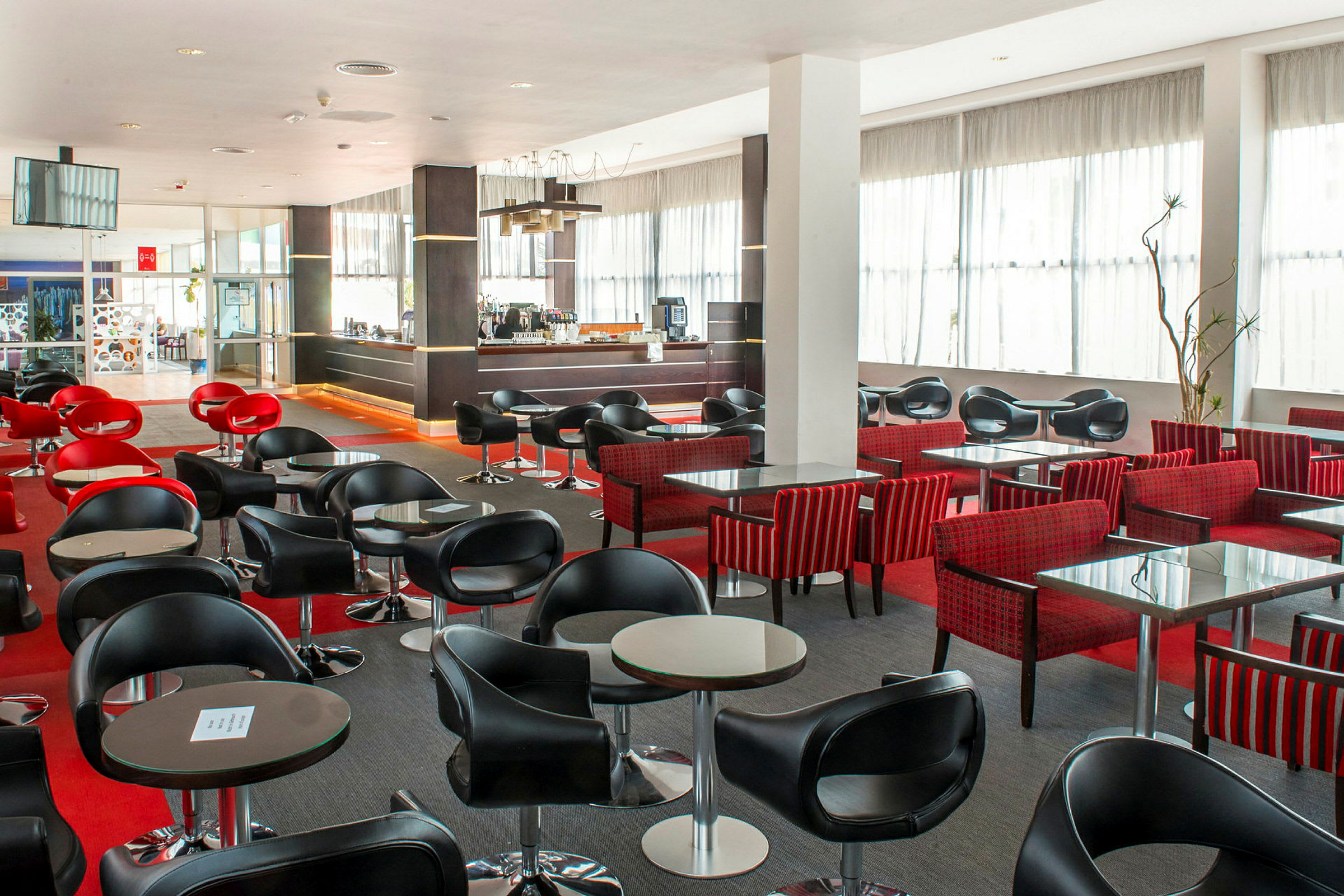 En moderne kafé- eller barområde med svarte og røde stoler og små bord. (AI-generert tekst)