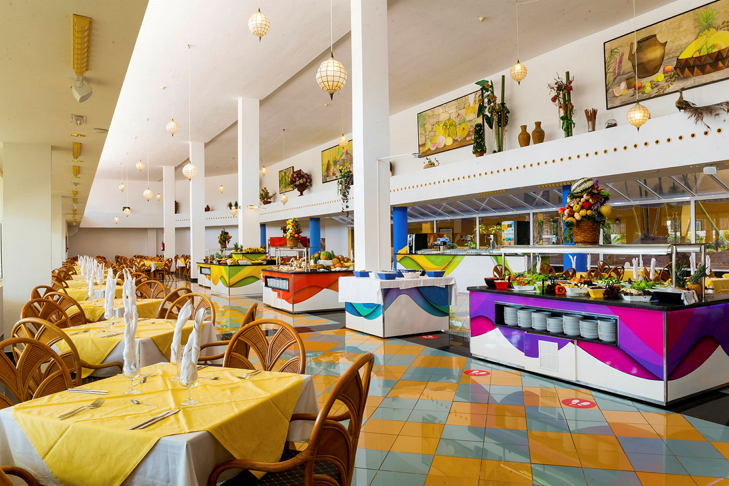 En romslig restaurant med luftige lokaler, gule duker på bordene og flere fargerike bufféstasjoner. (AI-generert tekst)