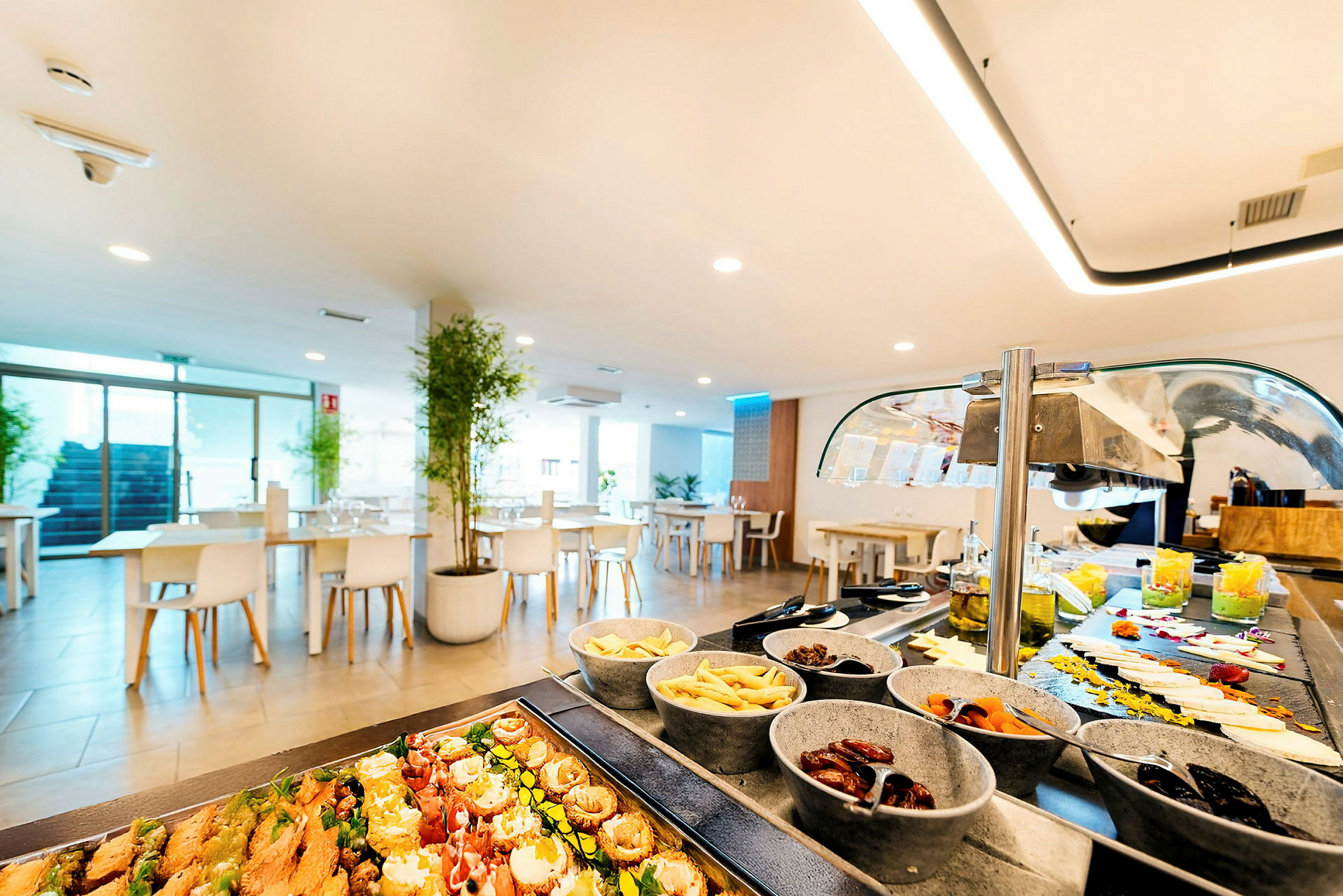 En lys restaurantinteriør med buffetbord fylt med ulike retter og små skåler. (AI-generert tekst)
