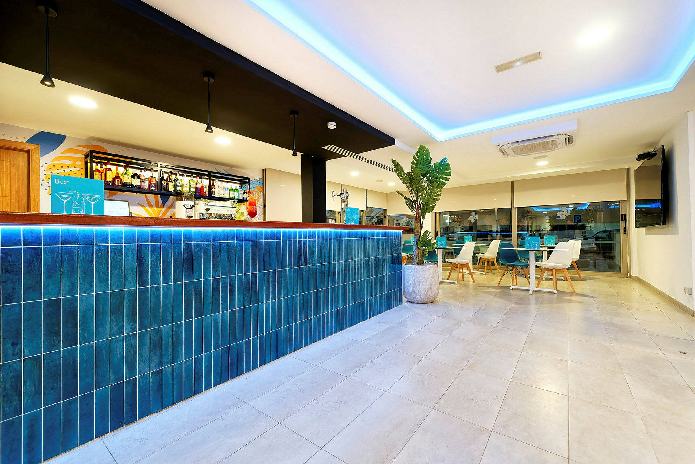 En moderne hotellbar med en blå flislagt bardisk og stilren innredning. I bakgrunnen sees sittegrupper og en stor vindusvegg. (AI-generert tekst)