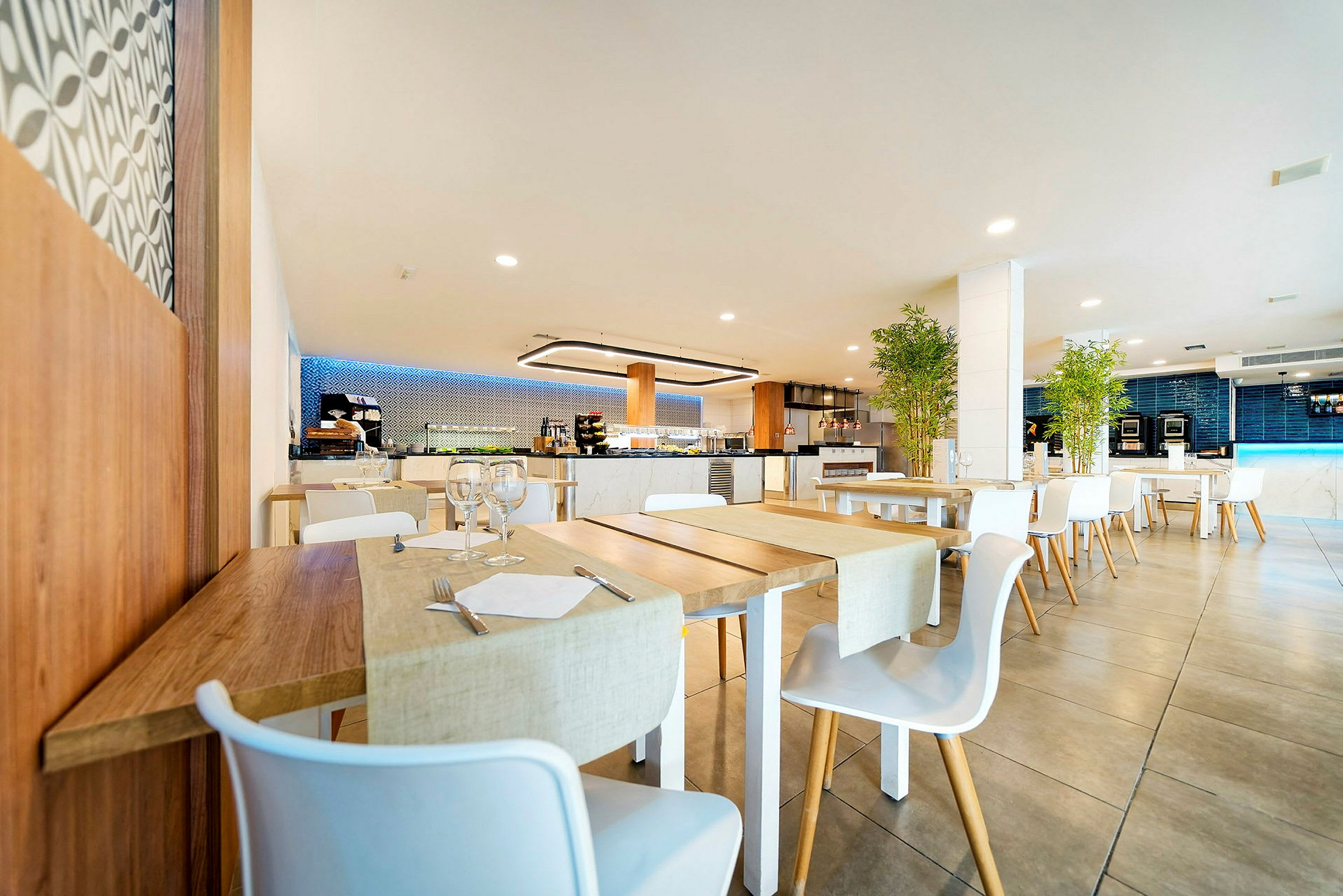 En moderne restaurantlokale med trebord og hvite stoler, dekorert med planter og myk belysning. (AI-generert tekst)