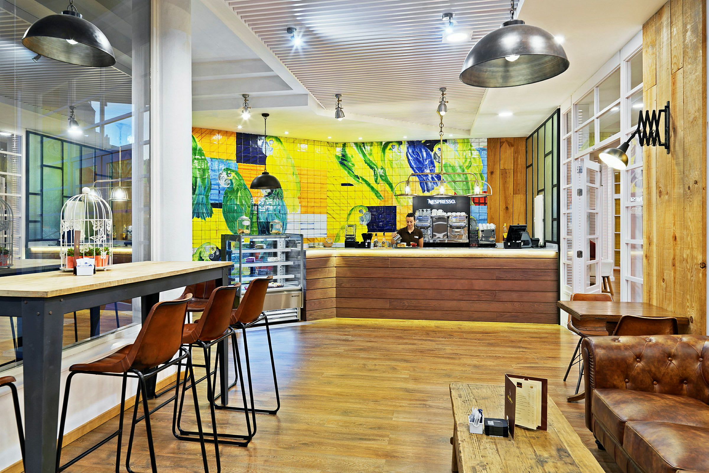 Interiør av en kafé med fargerikt flislagt vegg, høye stoler og tretak. (AI-generert tekst)