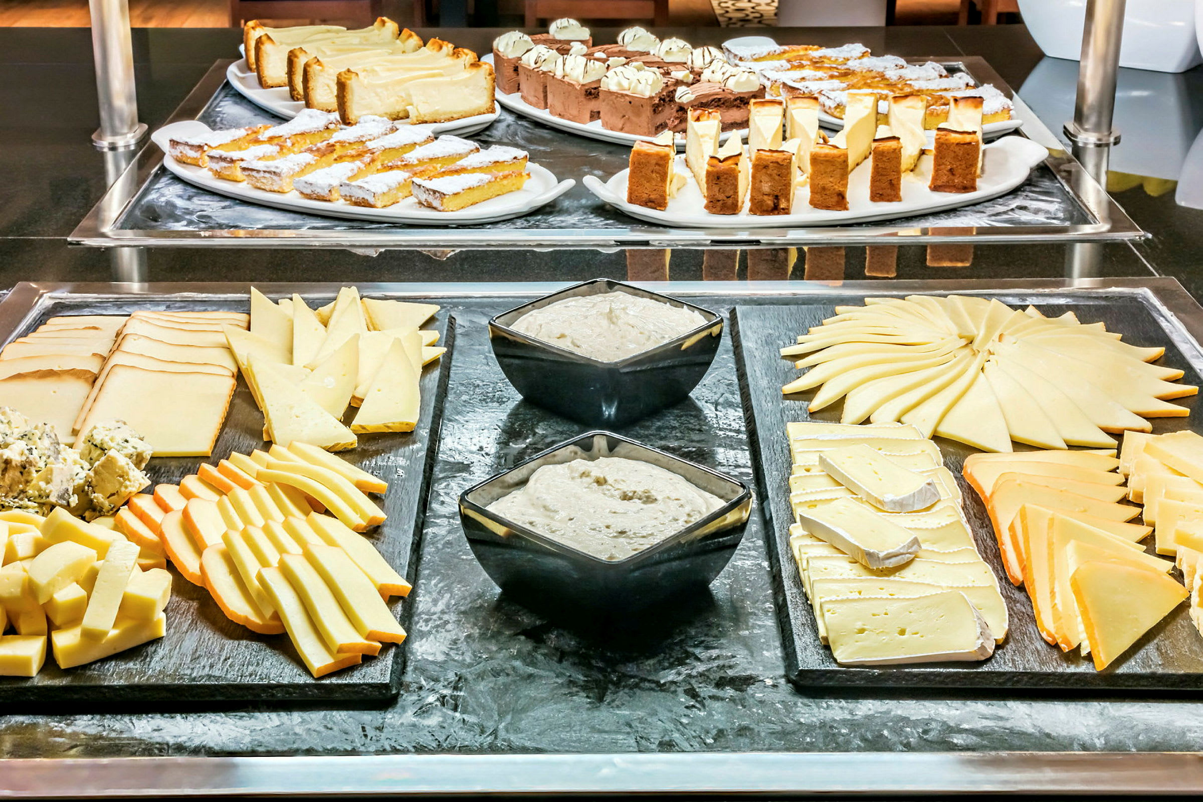 Bilde av en buffet med forskjellige typer ost, dip i skåler og bakverk på fat. (AI-generert tekst)