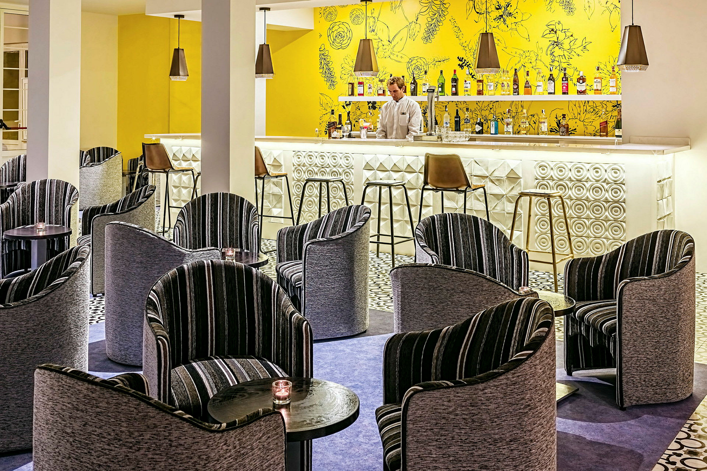En hotellbar med fargerik innredning, inkludert moderne stoler og små bord. (AI-generert tekst)