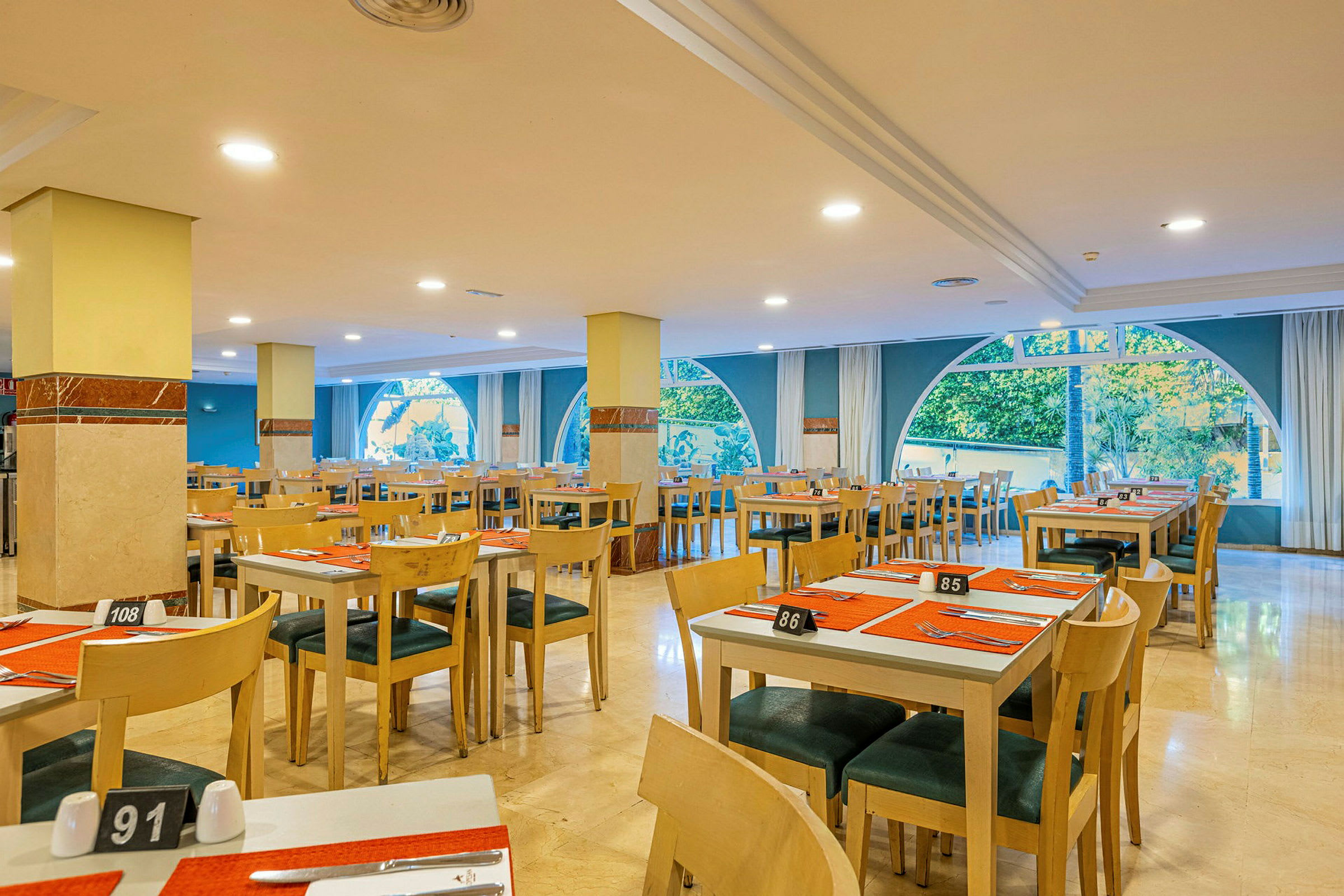 Interiør av en restaurant med dekkede bord og store vinduer. (AI-generert tekst)