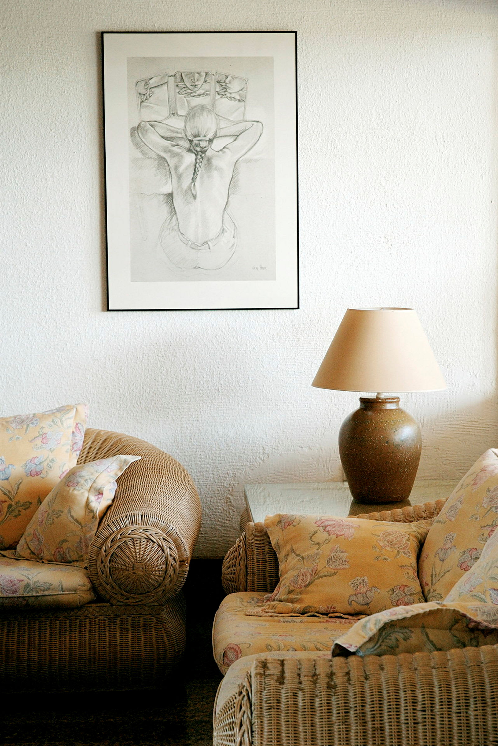 Bilde av en stueinteriør med et bilde på veggen, en lampe på et bord og rottingmøbler med blomstrete puter. (AI-generert tekst)