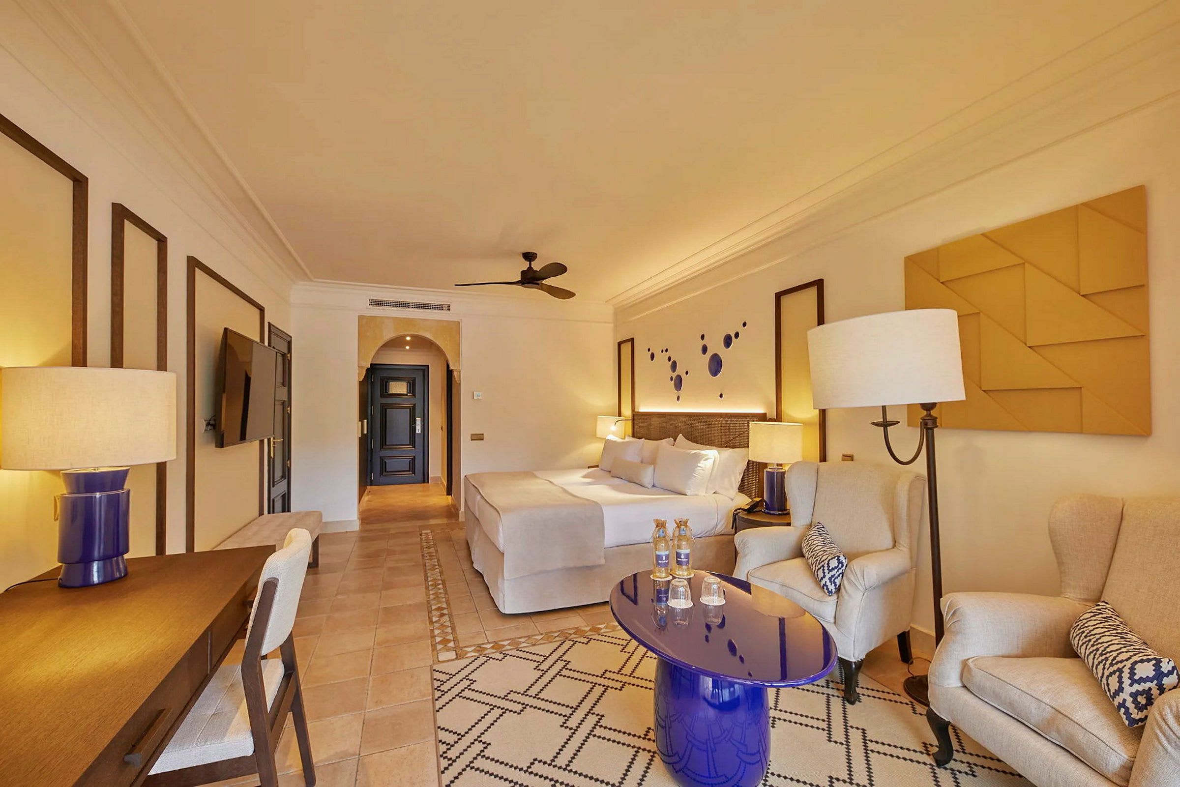 Et elegant innredet hotellrom med en stor seng, sittegruppe og skrivebord. (AI-generert tekst)