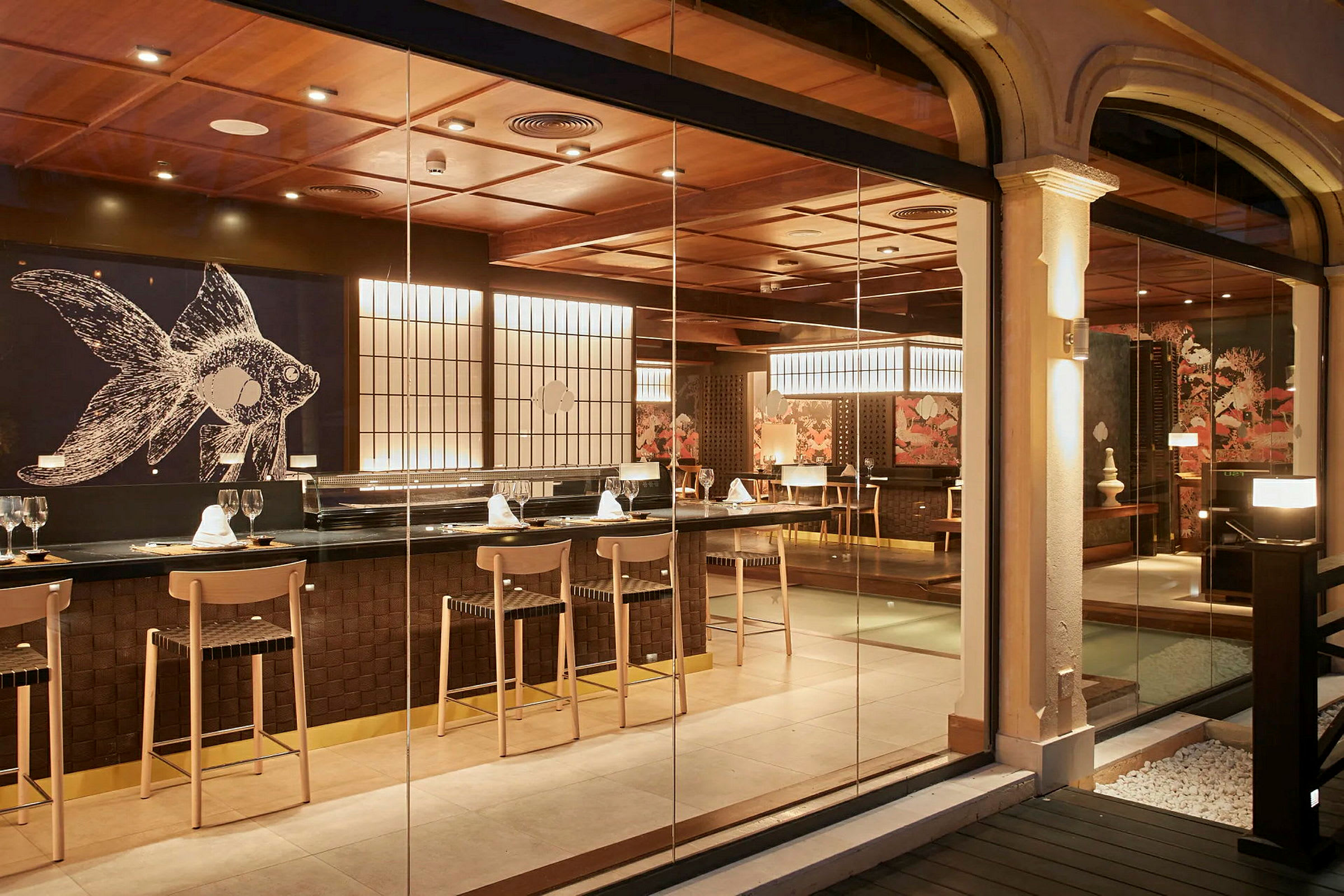 En elegant restaurant med en bar og sitteplasser. Det er en stor veggdekorasjon med et fiskemotiv og belysning som skaper en varm atmosfære. (AI-generert tekst)