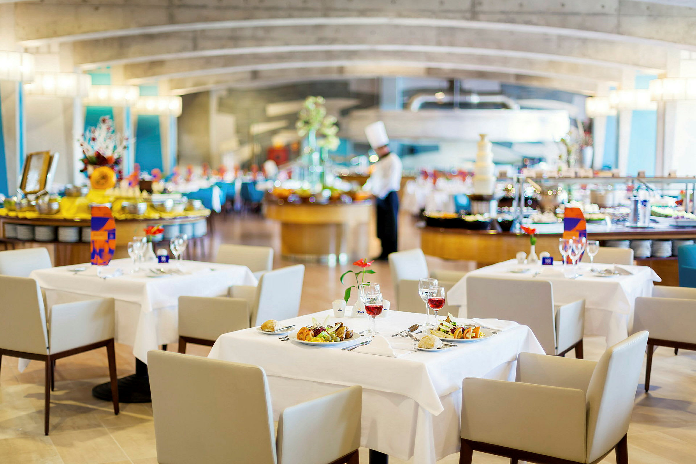 Restaurant med dekkede bord, serveringsområde og en kokk i bakgrunnen. (AI-generert tekst)