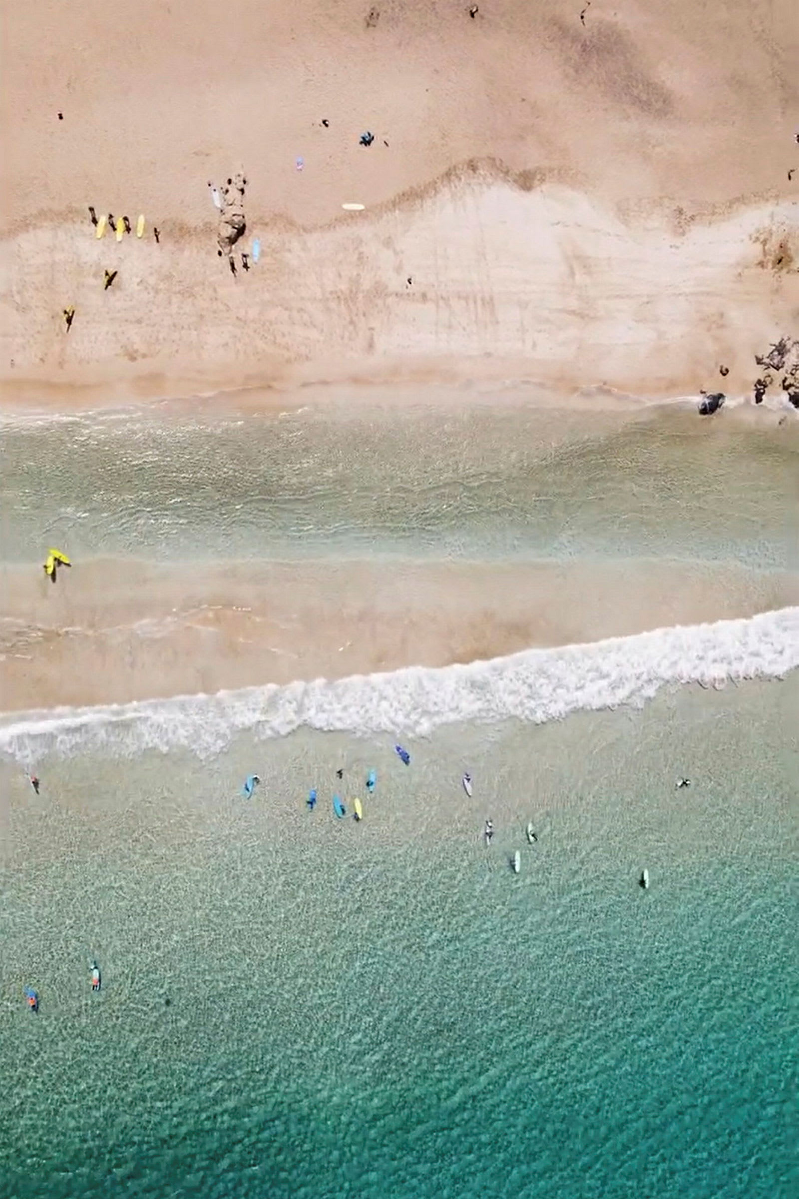 Flyfoto av en strand med mennesker, bølger og surfebrett i vannet. (AI-generert tekst)