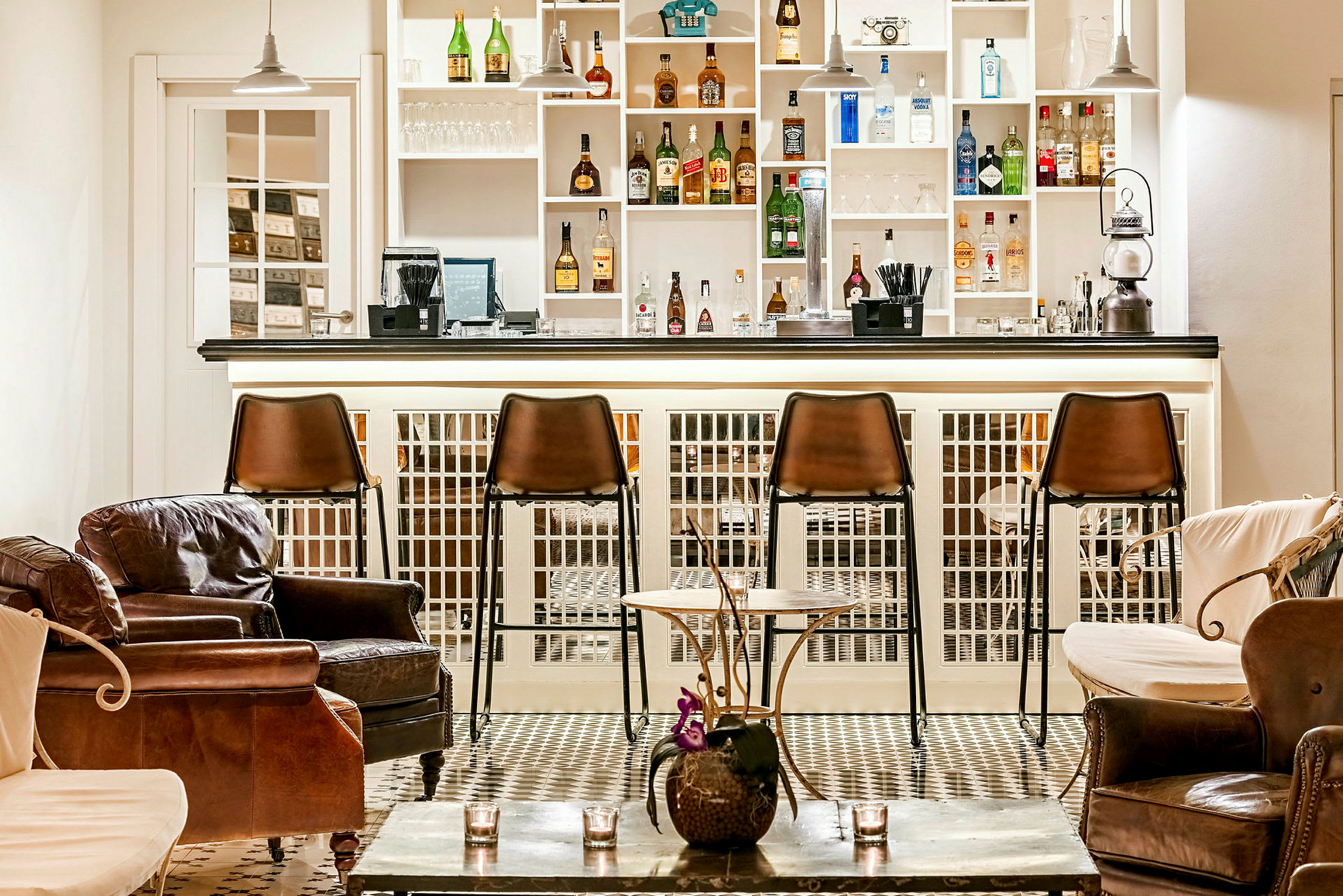 Bilde av en elegant bar med brune barstoler og komfortable skinnstoler. Hyllene bak disken er fylt med flasker og glass. (AI-generert tekst)