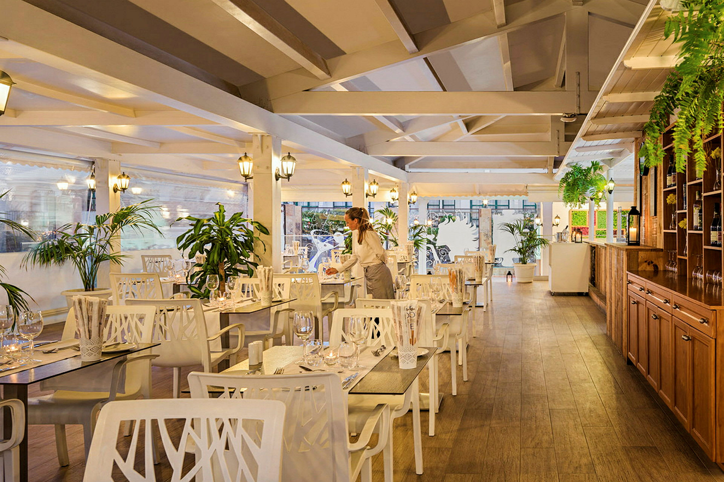 Interiør av en restaurant med treverk, hvite møbler og grønne planter. (AI-generert tekst)