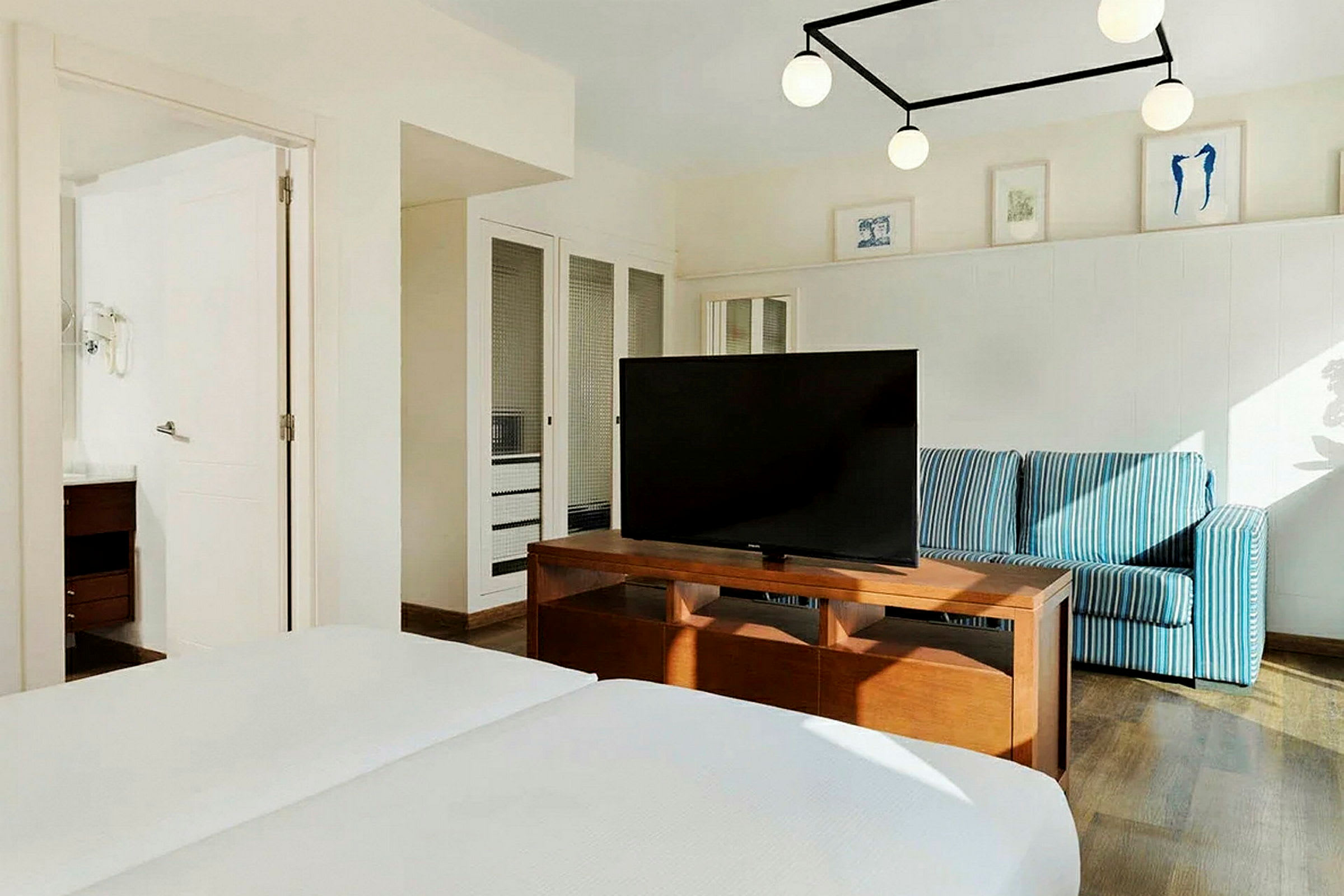 Et hotellrom med en dobbeltseng, en TV på et trebord, en blåstripet sofa og veggdekorasjoner. (AI-generert tekst)