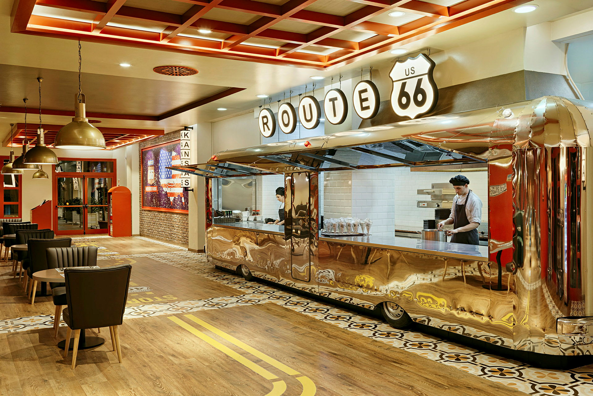 Et interiør av en restaurant med et retro-tema, hvor en serveringsdisk er utformet som en skinnende trailer, og flere spisebord og stoler er plassert rundt. (AI-generert tekst)