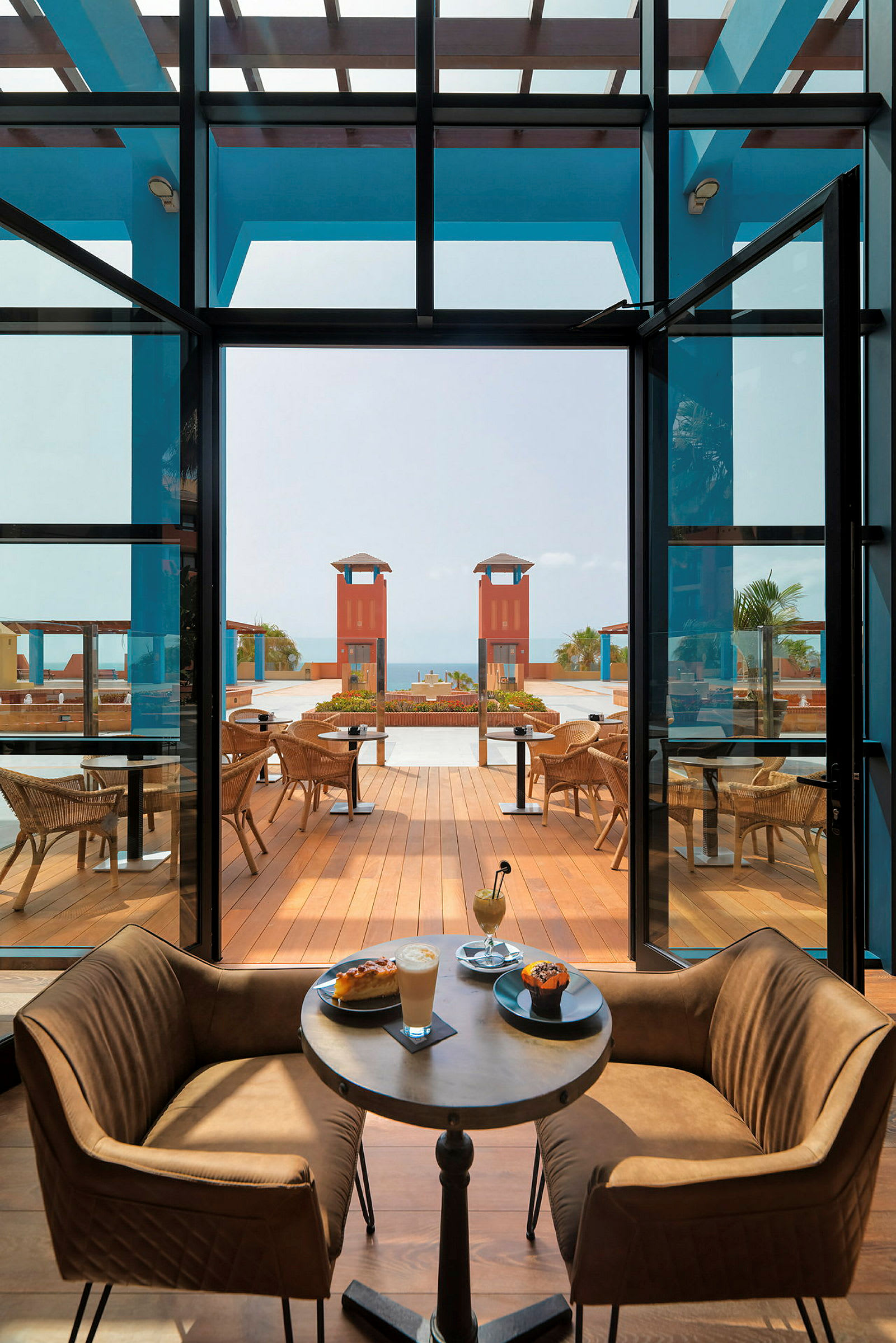 Interiør av en restaurant med bord og stoler, med vakker utsikt over en terrasse og havet. (AI-generert tekst)