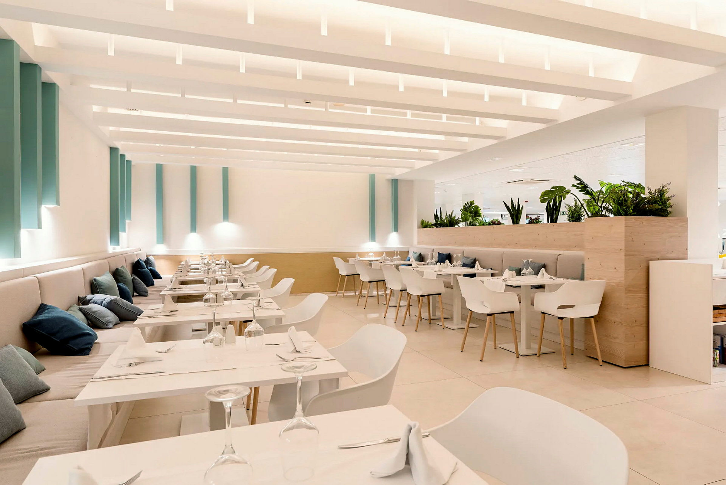 Et lyst og moderne innredet restaurantområde med hvite møbler og grønne planter. (AI-generert tekst)