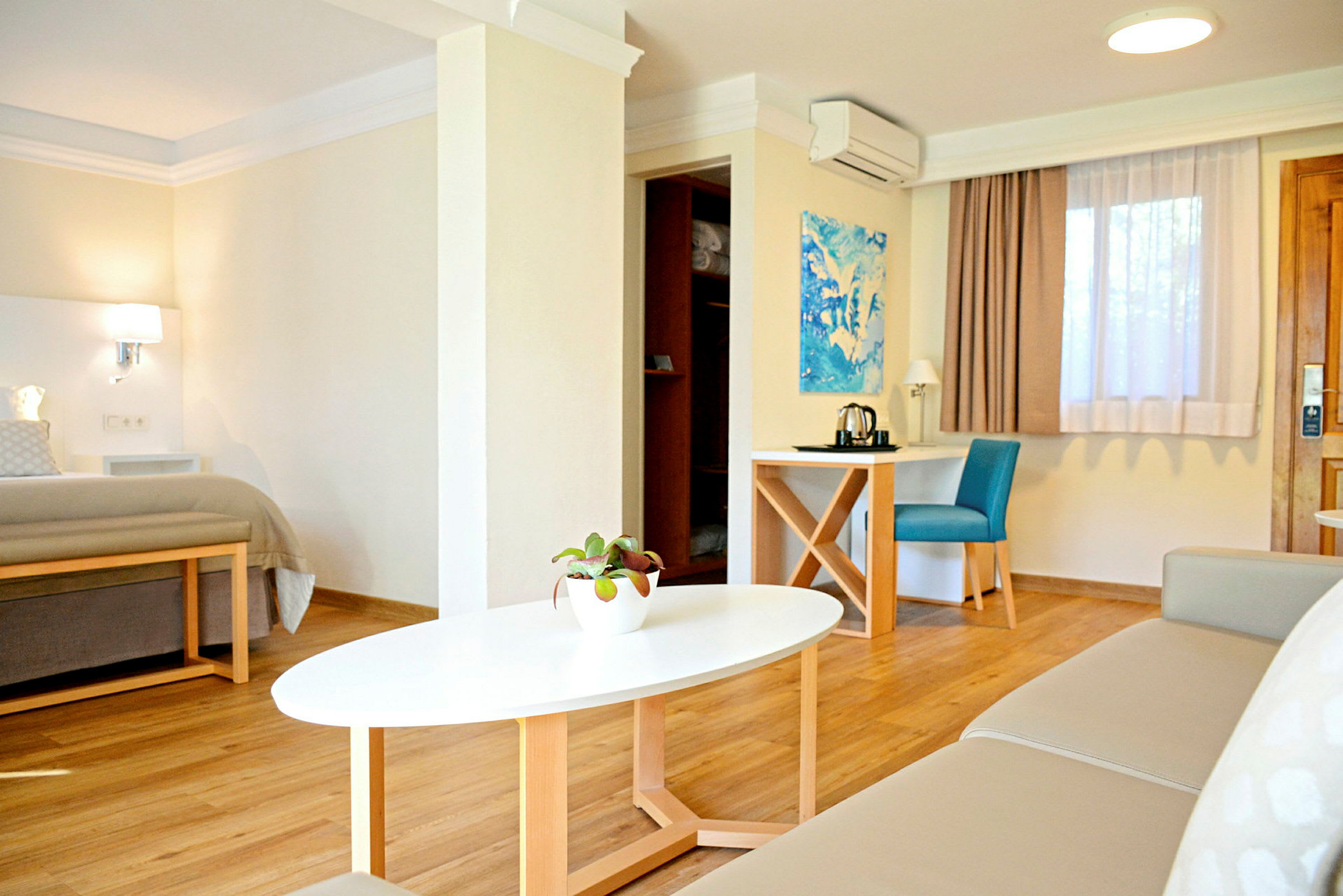 Et moderne og lyst hotellrom med en seng, en sofa, et salongbord og et skrivebord med en stol. (AI-generert tekst)