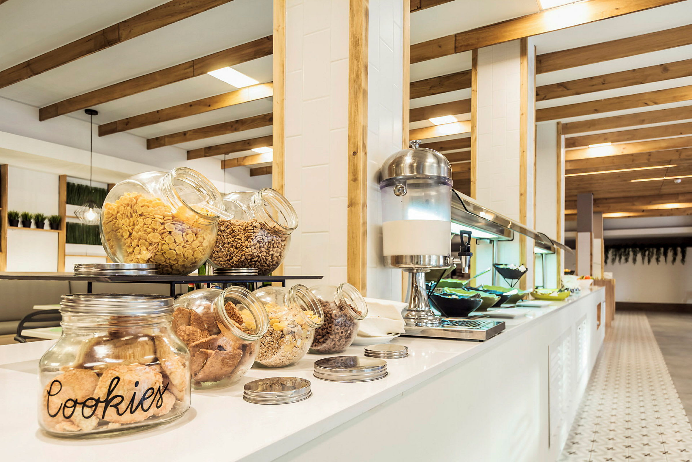 Glasskrukker med kjeks og frokostblandinger står fremme på en hvit benk ved en bufféservering. (AI-generert tekst)