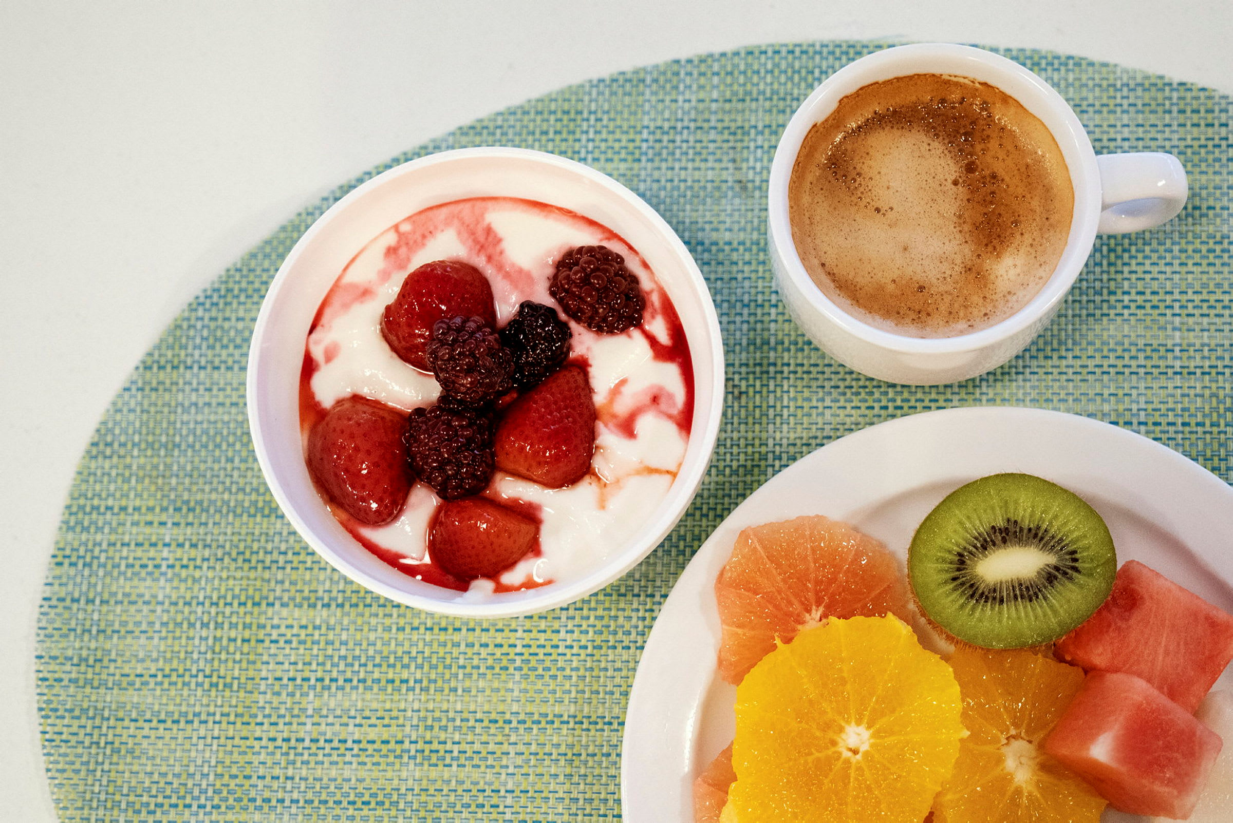 En frokost med yoghurt toppet med bær, en kopp kaffe og oppskåret frisk frukt. (AI-generert tekst)
