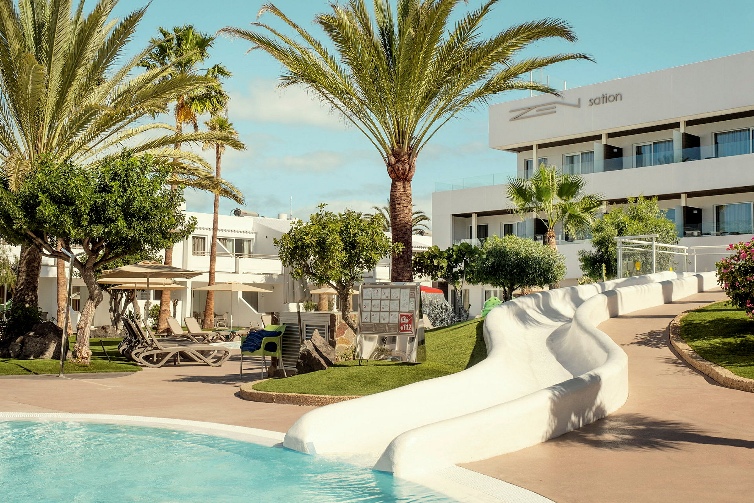 Hotellbassengets område med grønne omgivelser, solsenger og en vannsklie. (AI-generert tekst)