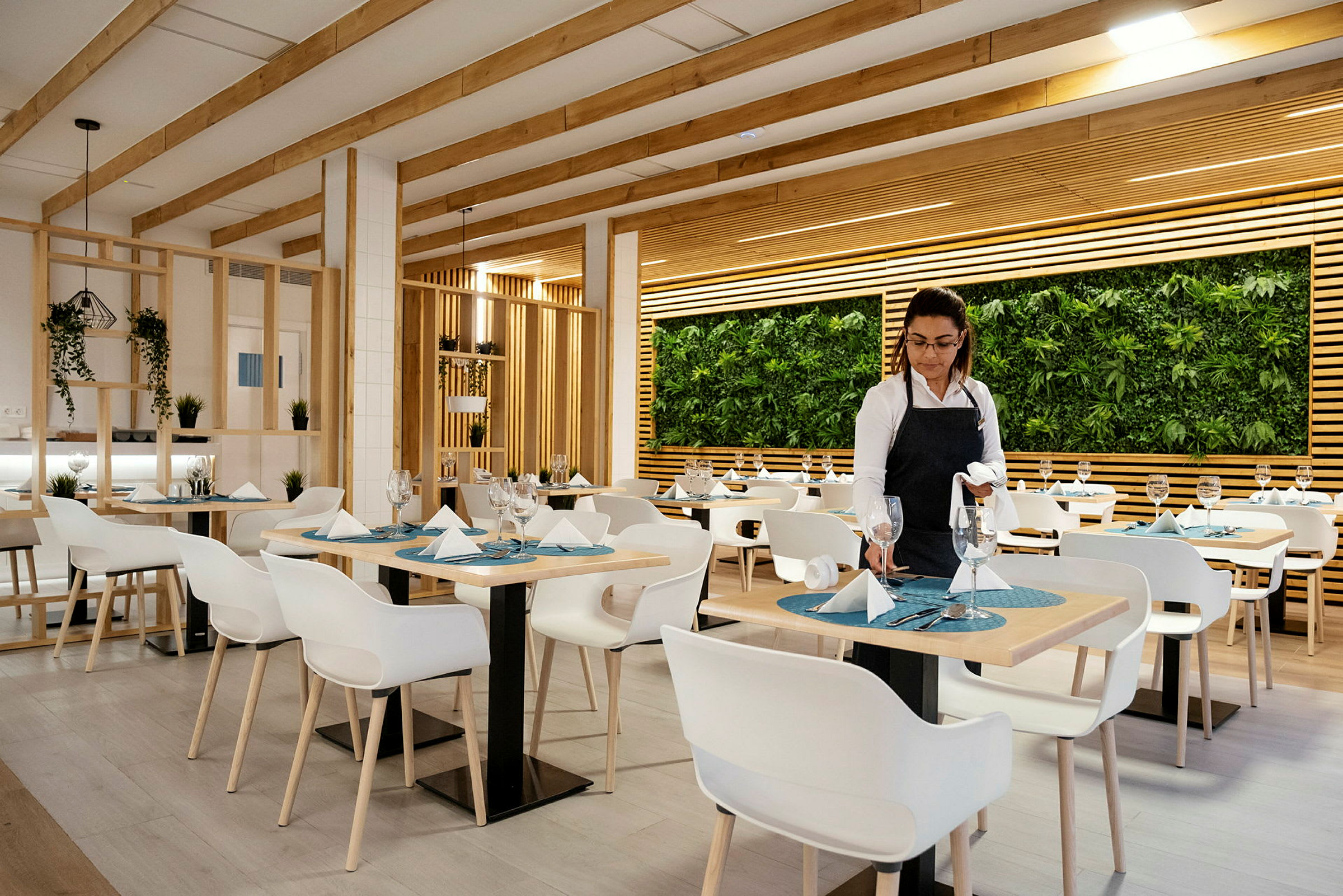 En restaurant med moderne innredning med hvite stoler, dekkede bord og en vegg dekorerte med planter. (AI-generert tekst)
