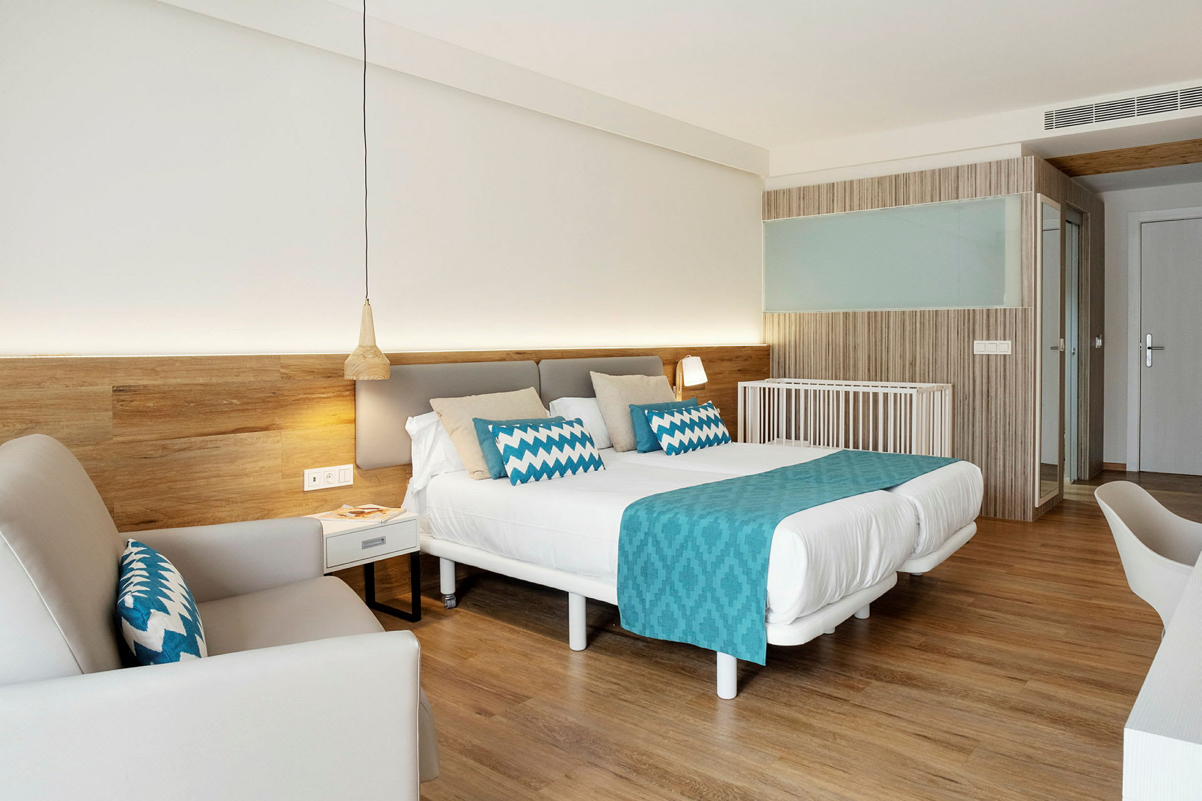 Et godt opplyst hotellrom med en dobbeltseng, blå dekorasjoner og tretrekk. (AI-generert tekst)