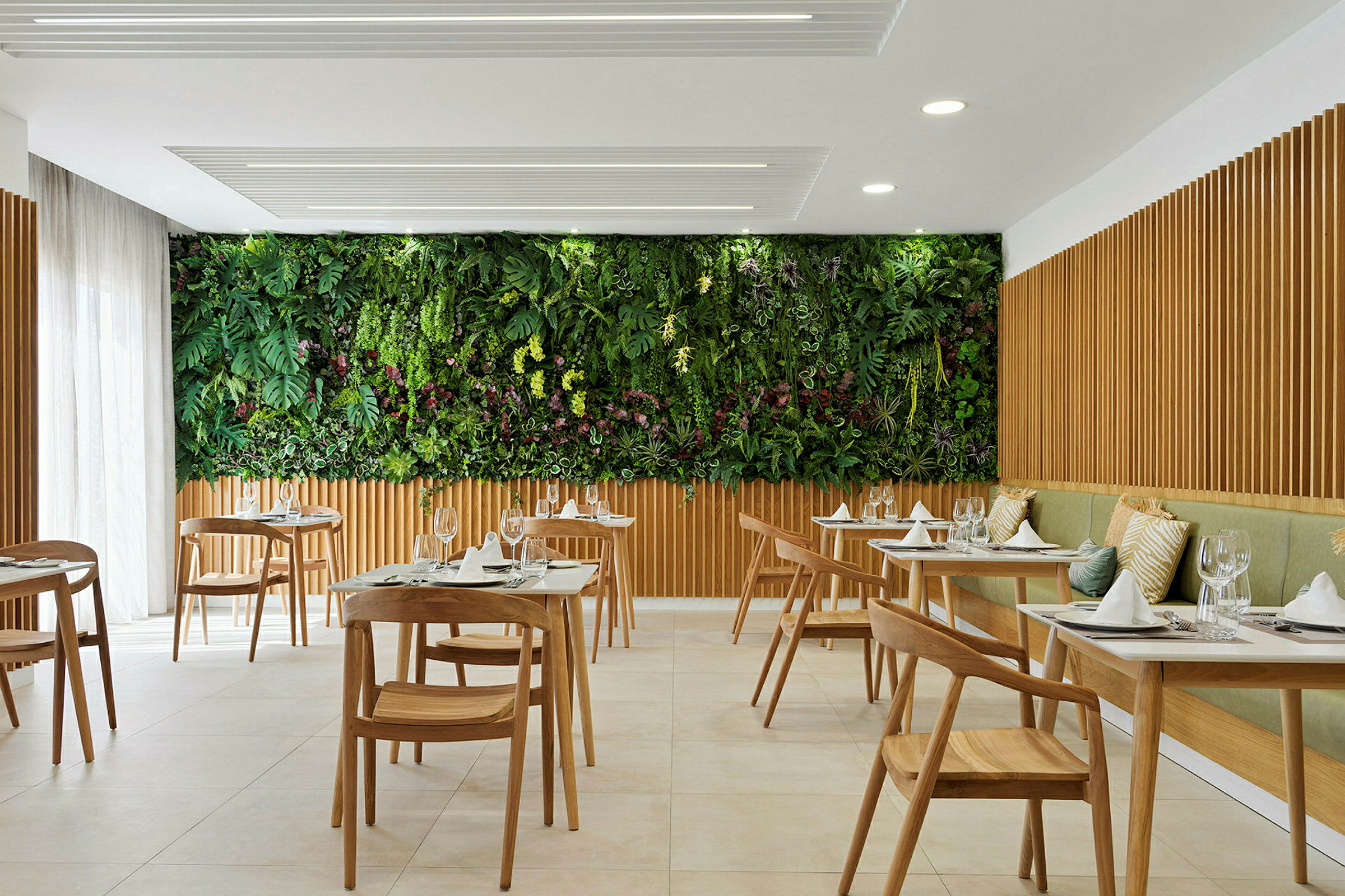 En moderne restaurant med trebord og stoler, samt en grønn vegg med planter. (AI-generert tekst)