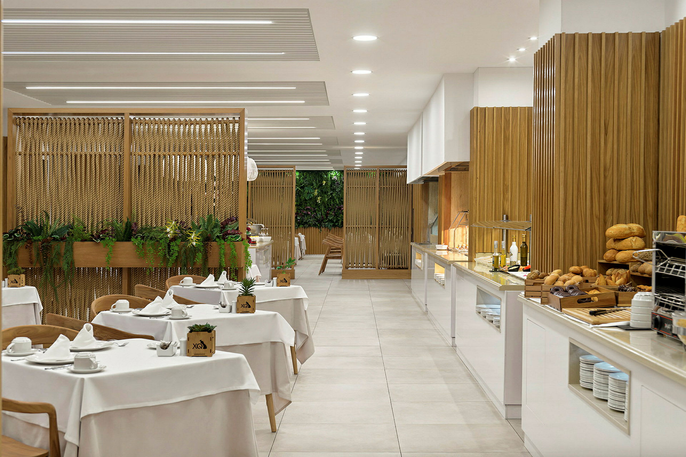 Restaurant med dekkede bord og en buffet med brød og oljer, samt en dekorativ vegg med planter. (AI-generert tekst)