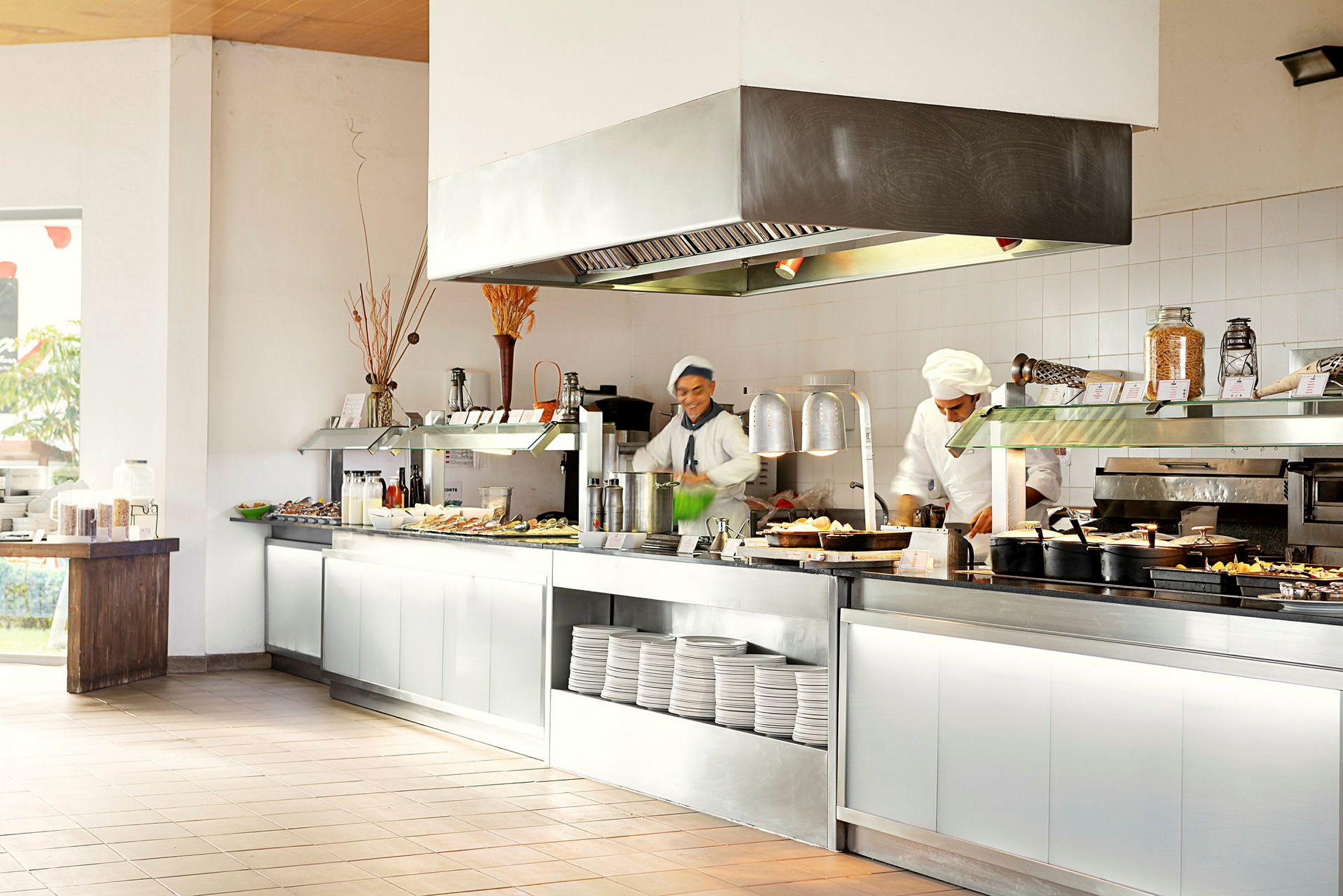 En restaurantbuffet med ulike retter og tallerkener plassert på et serveringsbord. Kokker tilbereder mat. (AI-generert tekst)