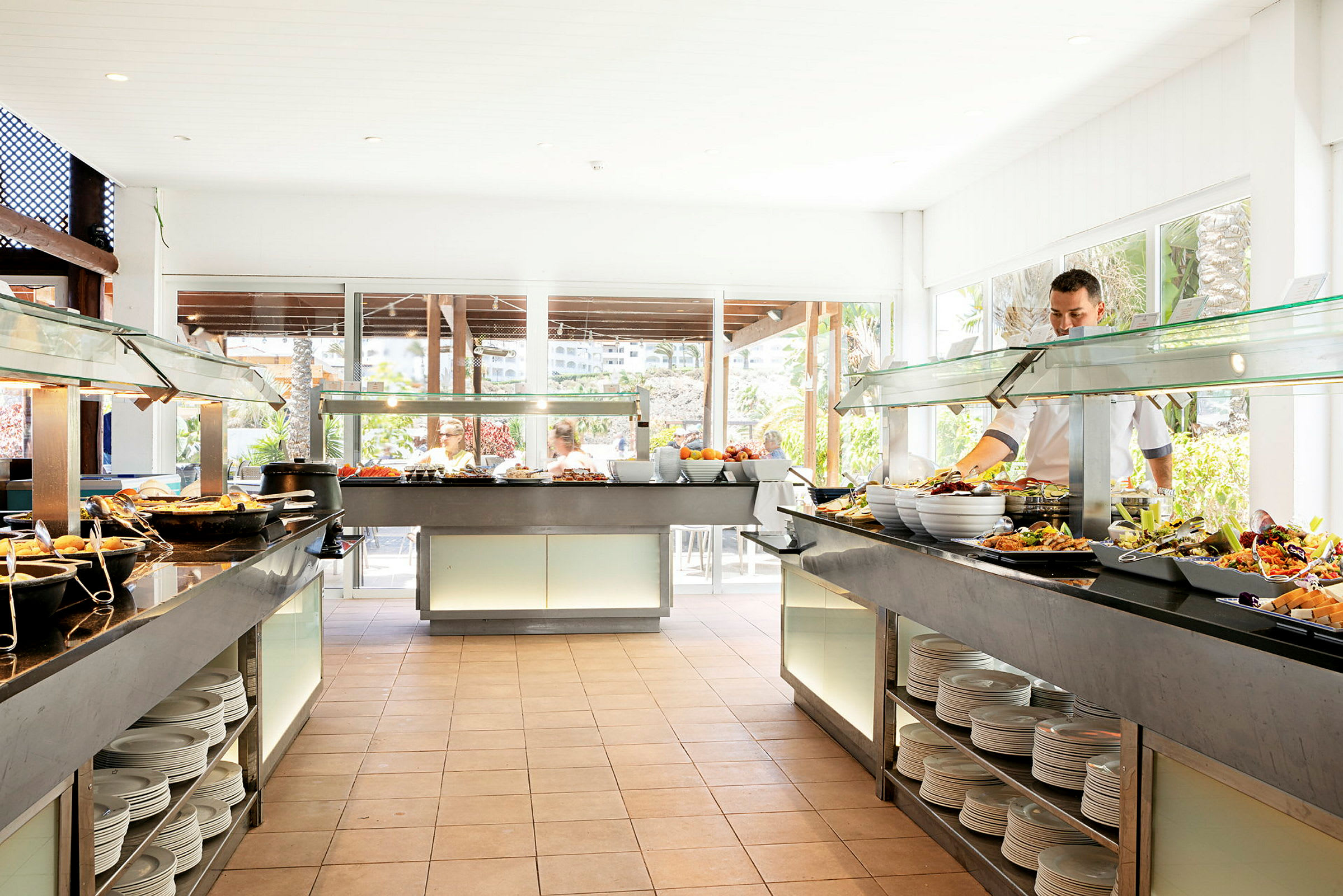 En buffet med ulike retter plassert i et lyst rom med store vinduer. (AI-generert tekst)